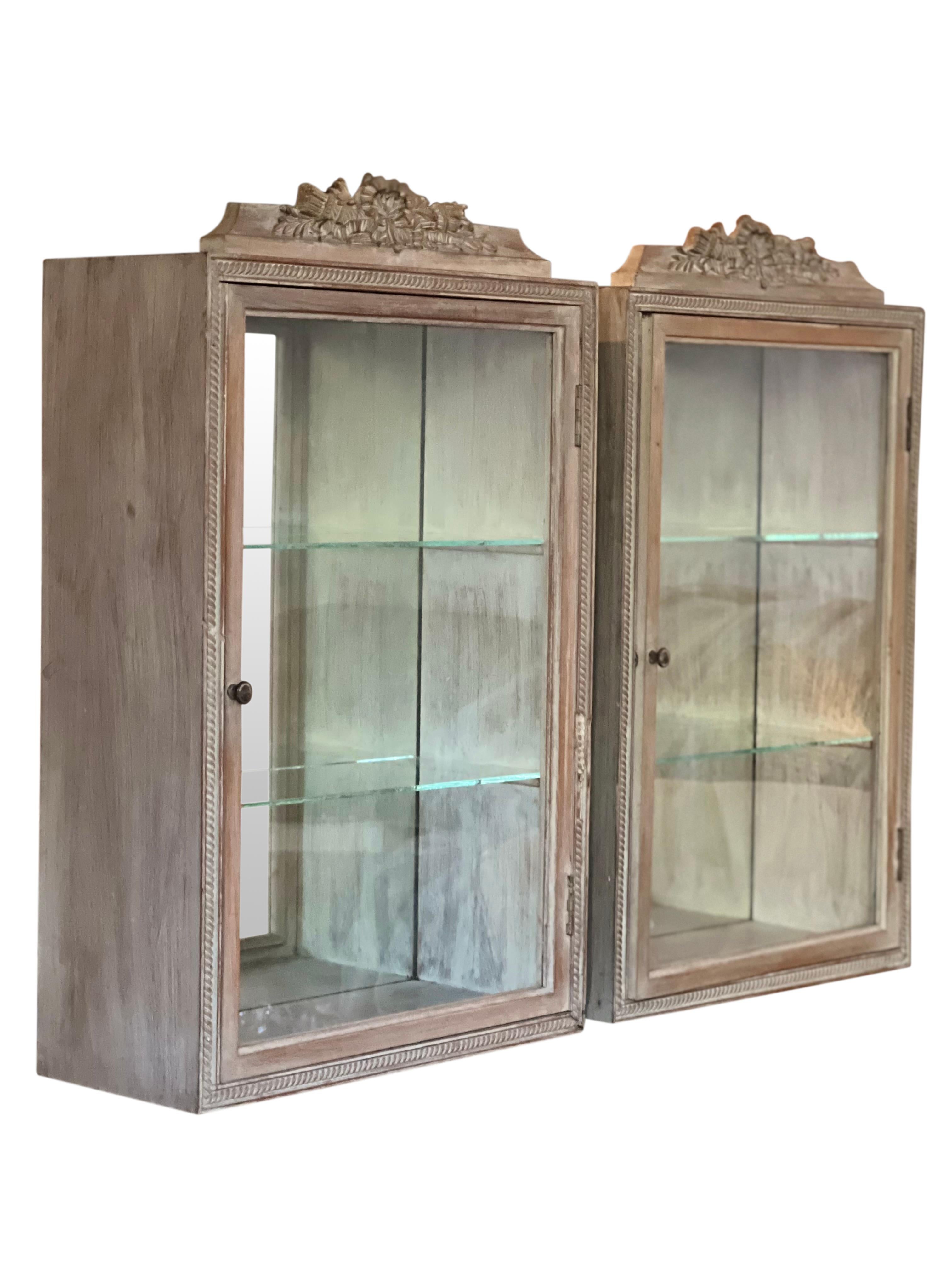 Gorgeous vintage Venetian hand painted and carved mirrored wall cabinets, early 20th century.

The cabinets feature a mirrored back and two glass shelves each. Intricately carved details of rope trim and a floral bouquet crest crafted from plaster