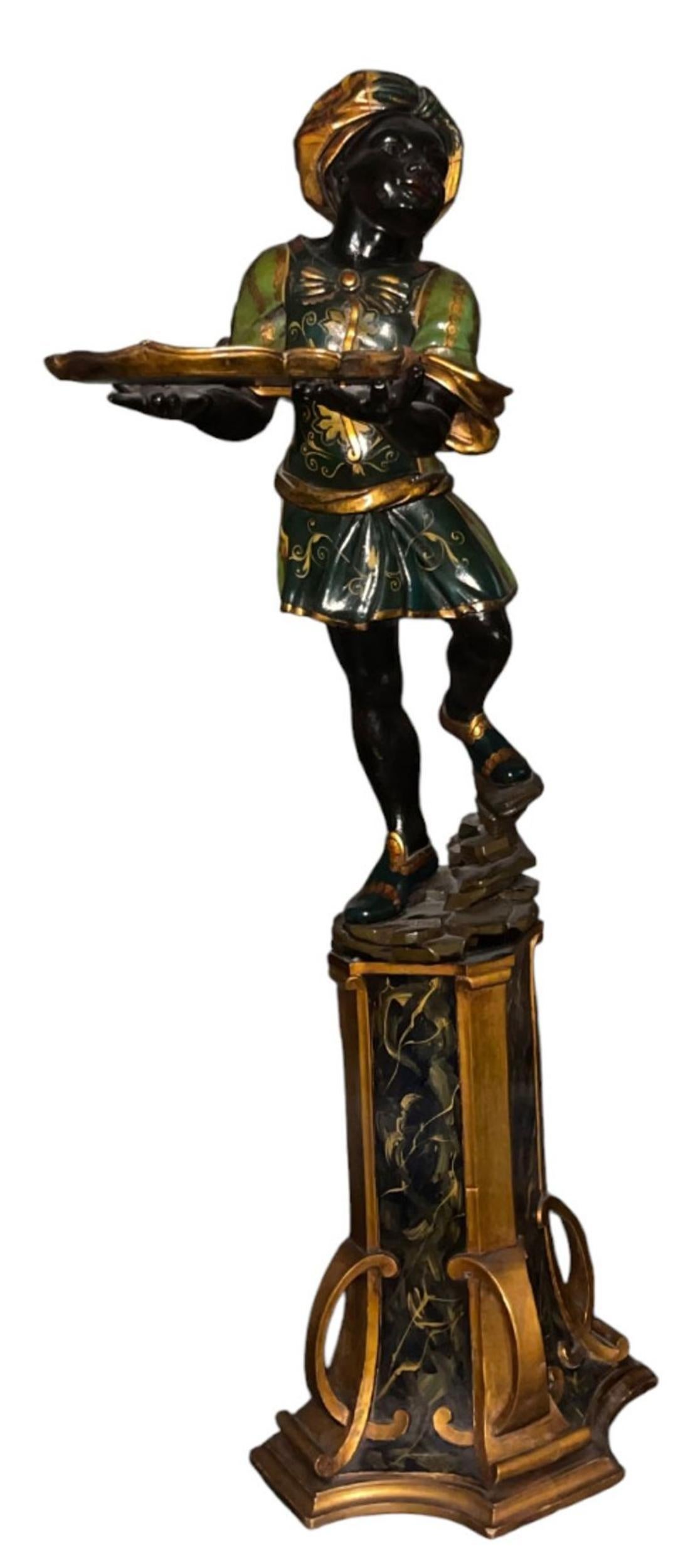 A striking pair of early 20th-century Italian polychrome carved wood Blackamoor figures, each finely modeled and richly decorated. The figures are depicted in dynamic, graceful poses, standing on naturalistic rocky bases and holding shallow