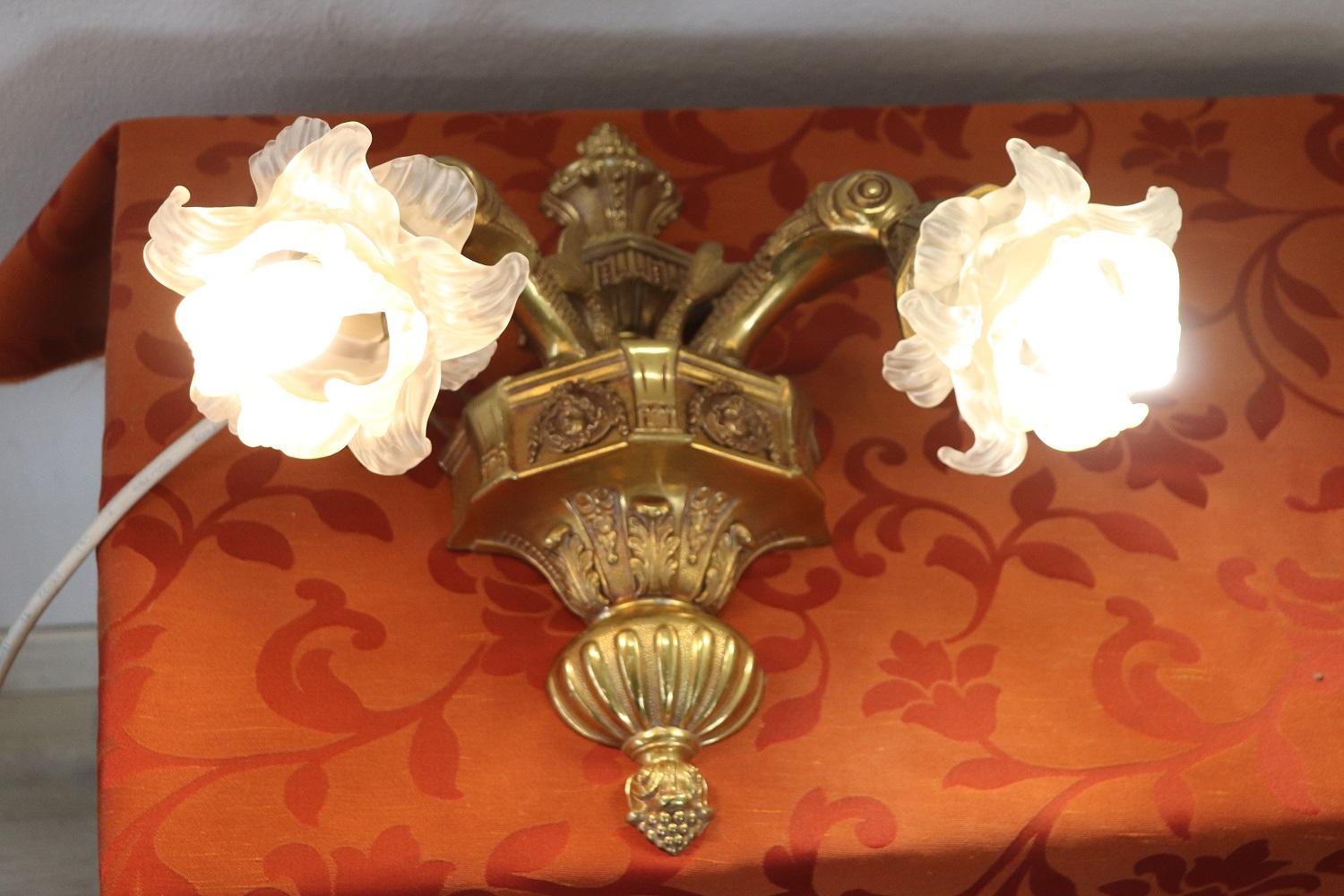 Beautiful and refined Italian early 20th century pair of wall lights or sconces two lights each. Made of golden bronze. The bronze is finely chiseled with elaborate decoration. Large and beautiful glass flowers hide the bulb. Very decorative perfect