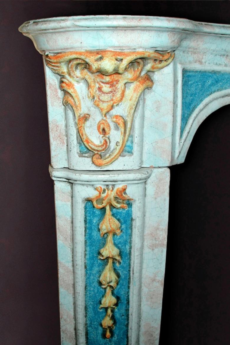 This fantastically unique polychrome ceramic mantel is made in the Louis XV style and features a coat of arms at center. The antique italian piece dates back to the early 20th century and sports leaves on either end of the apron. More detailed,