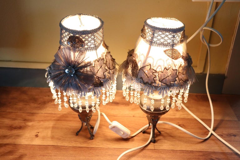 Delicious pair of small table lamps made of silver metal with small chiseled feet. The cloth hat decorated by hand with small pendants. Perfect for your bedside table. Electrical system not new but working.