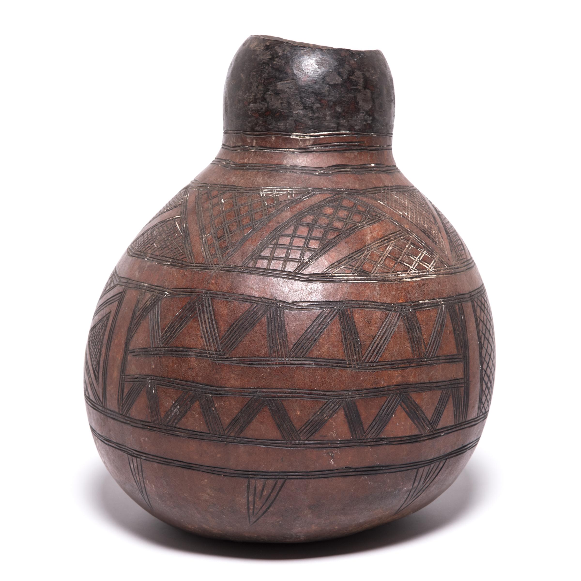 Nupe women were well-known for their skill in shaping drinking vessels. Everyday objects, like this gourd water vessel, received detailed attention. Made of a dried-out gourd, the vessel's varied textures come from its functional design. The