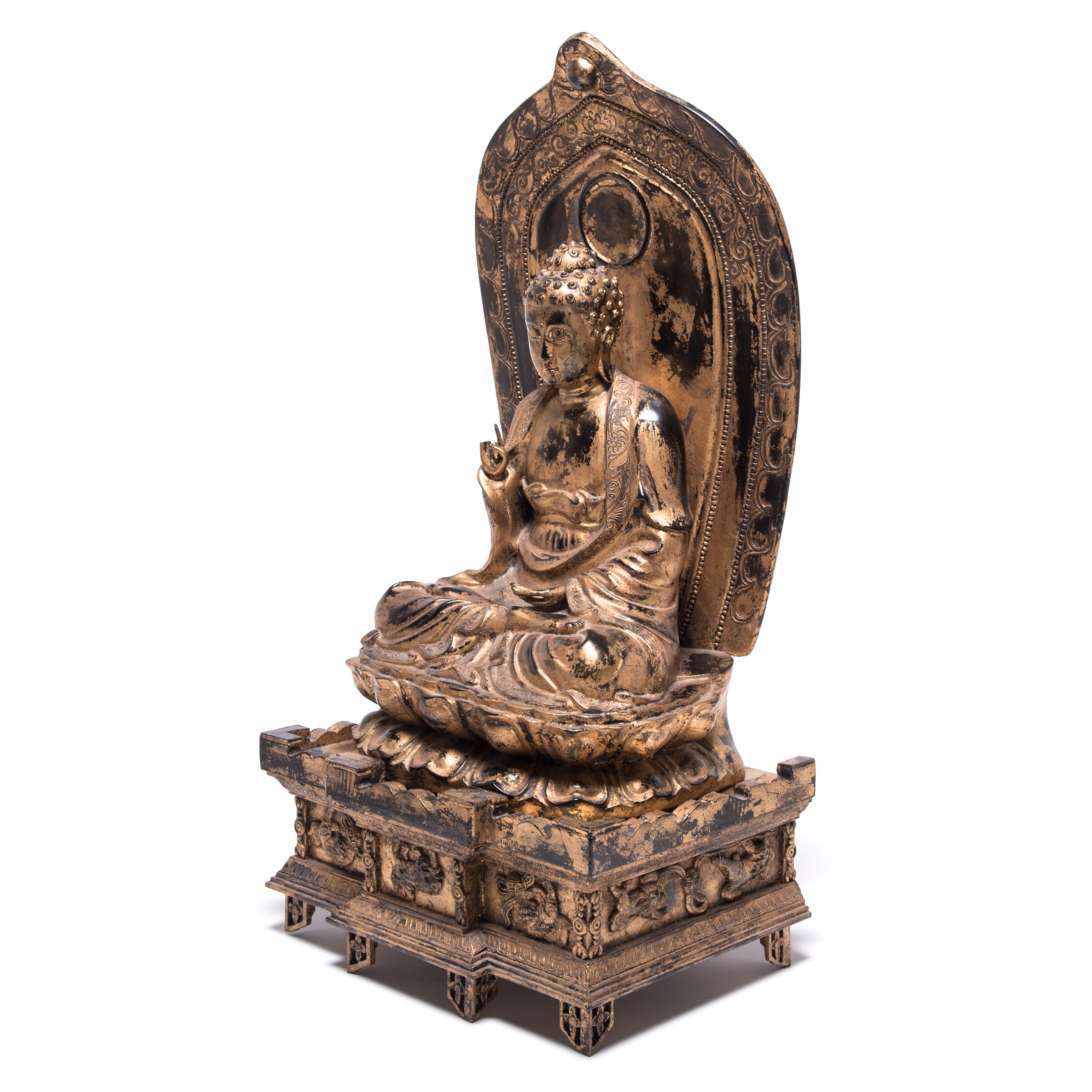 Intricately carved from wood, this exquisite Buddha was finished with gold leaf and lacquer. Adorned with guardian lion dogs playing with embroidered balls, an ornate, architectural base supports the lotus blossom on which the Buddha rests. Backed