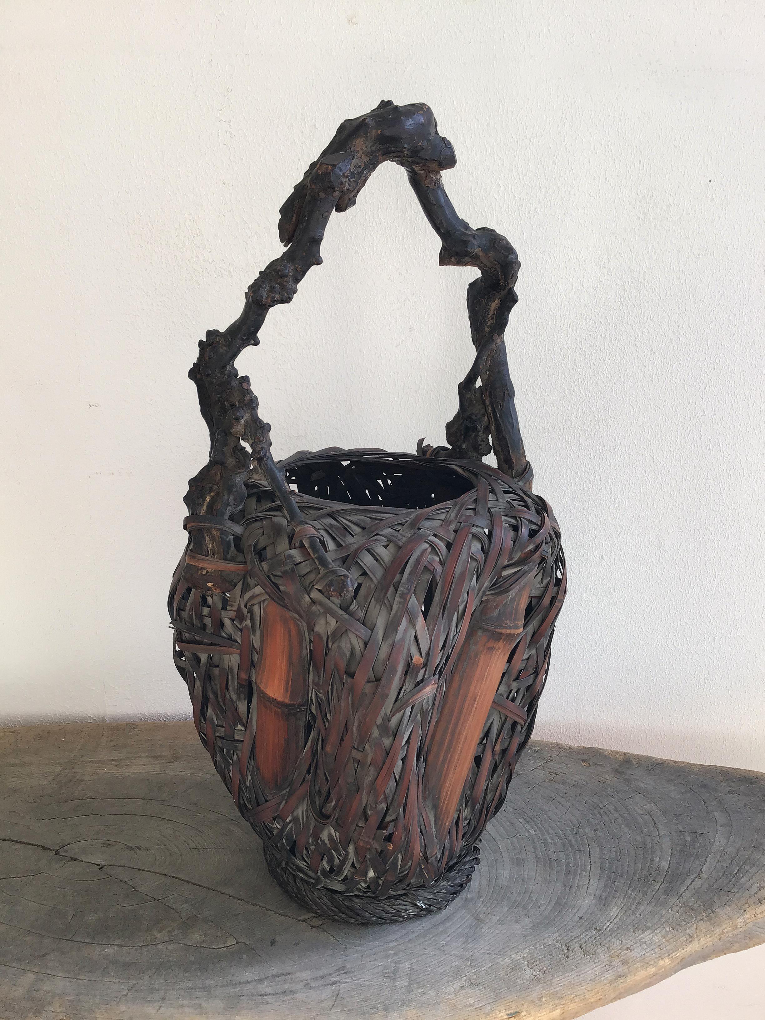 Flower basket as old Japanese ikebana vase made of wildly but refinedly woven two different type (condition) of bamboo attached with natural wood handle, early 20th century, approx. H 46 x 23 x 19 cm (18.11 x 9.05 x 7.48in). The bottom is holed as