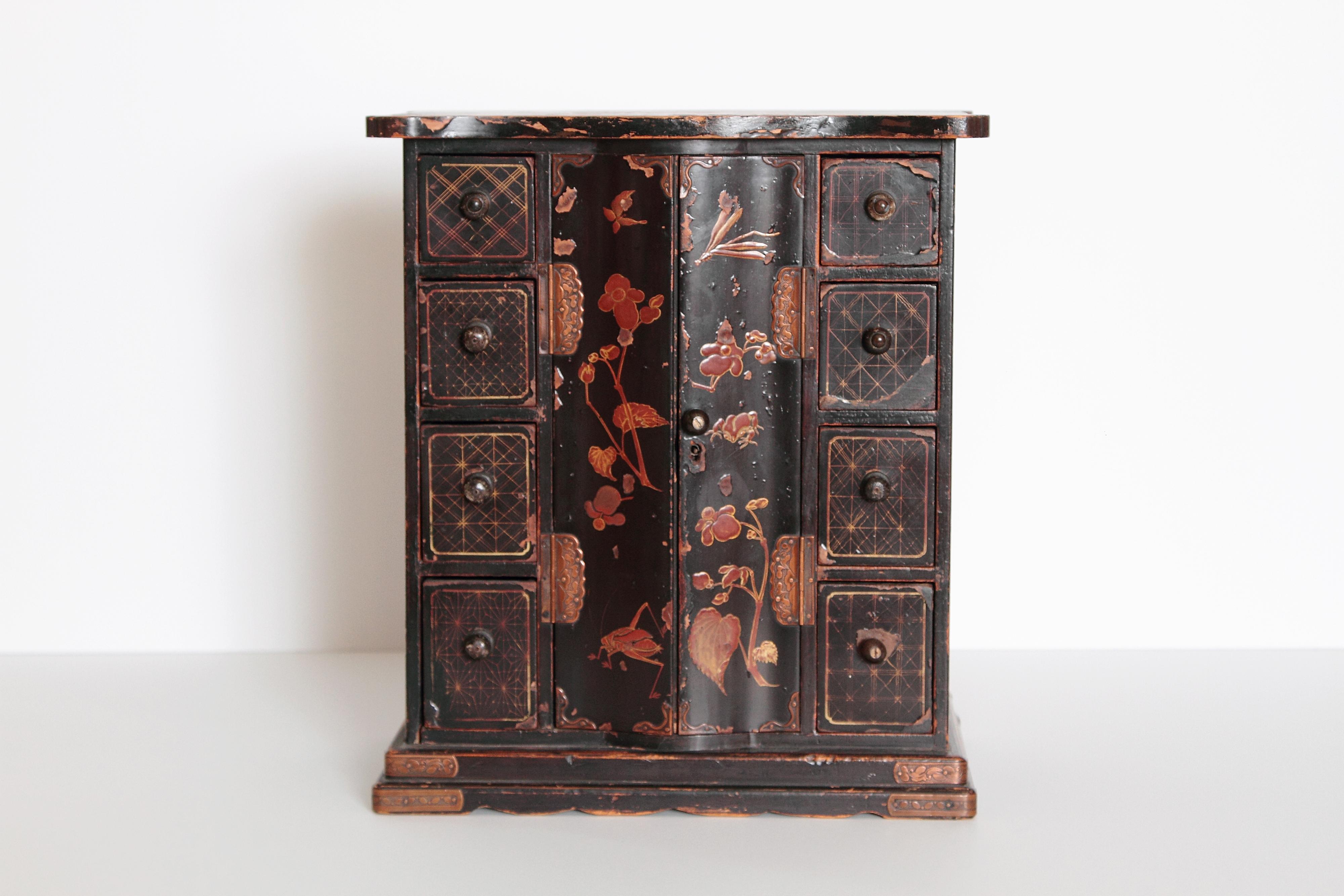 This early 20th century Japanese jewelry box is made of black lacquer and decorated with beautiful floral detailing. This piece still contains the original hardware and shows wear consistent with its age.
