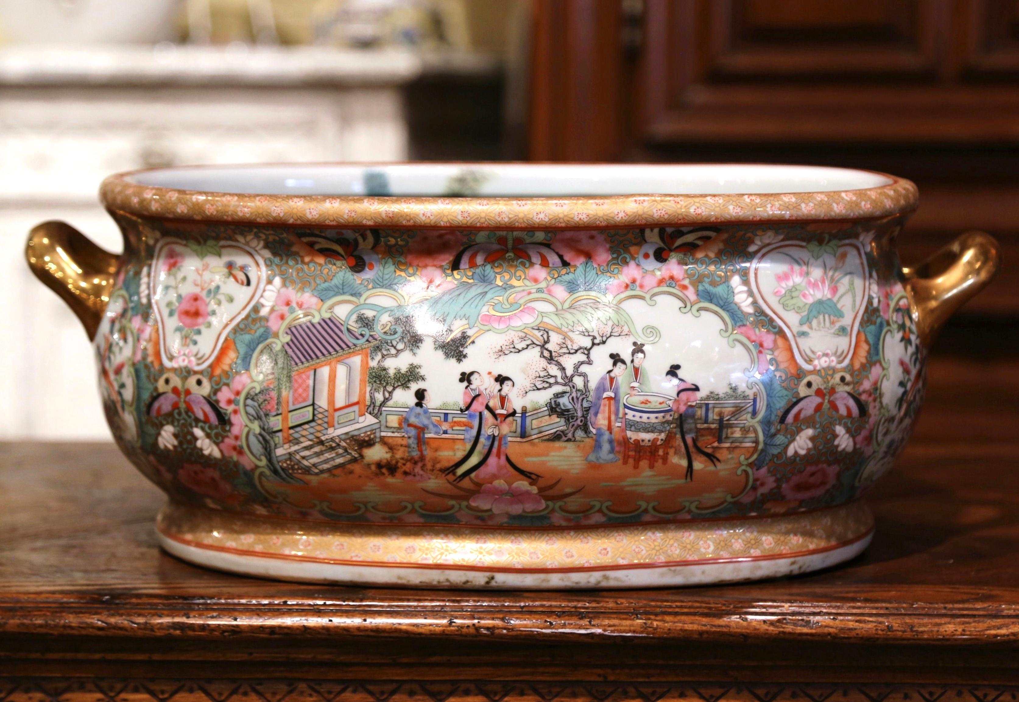 Crafted in Japan circa 1920 and oval in shape, the colorful porcelain basin with two side gilt handles bowl is hand painted with floral motifs including two medallions with Japanese people dressed in traditional clothing; the large bowl is further