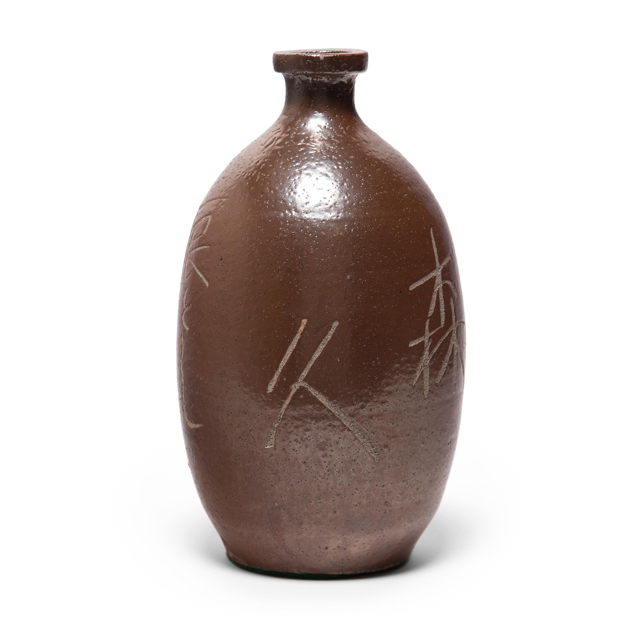 This glazed ceramic jar is a Japanese sake bottle from the late-Meiji era. The jar has a rounded bottleneck form and is coated with a warm brown glaze in resemblance to bizen ware pottery. Across the jar's sides, characters denoting details of
