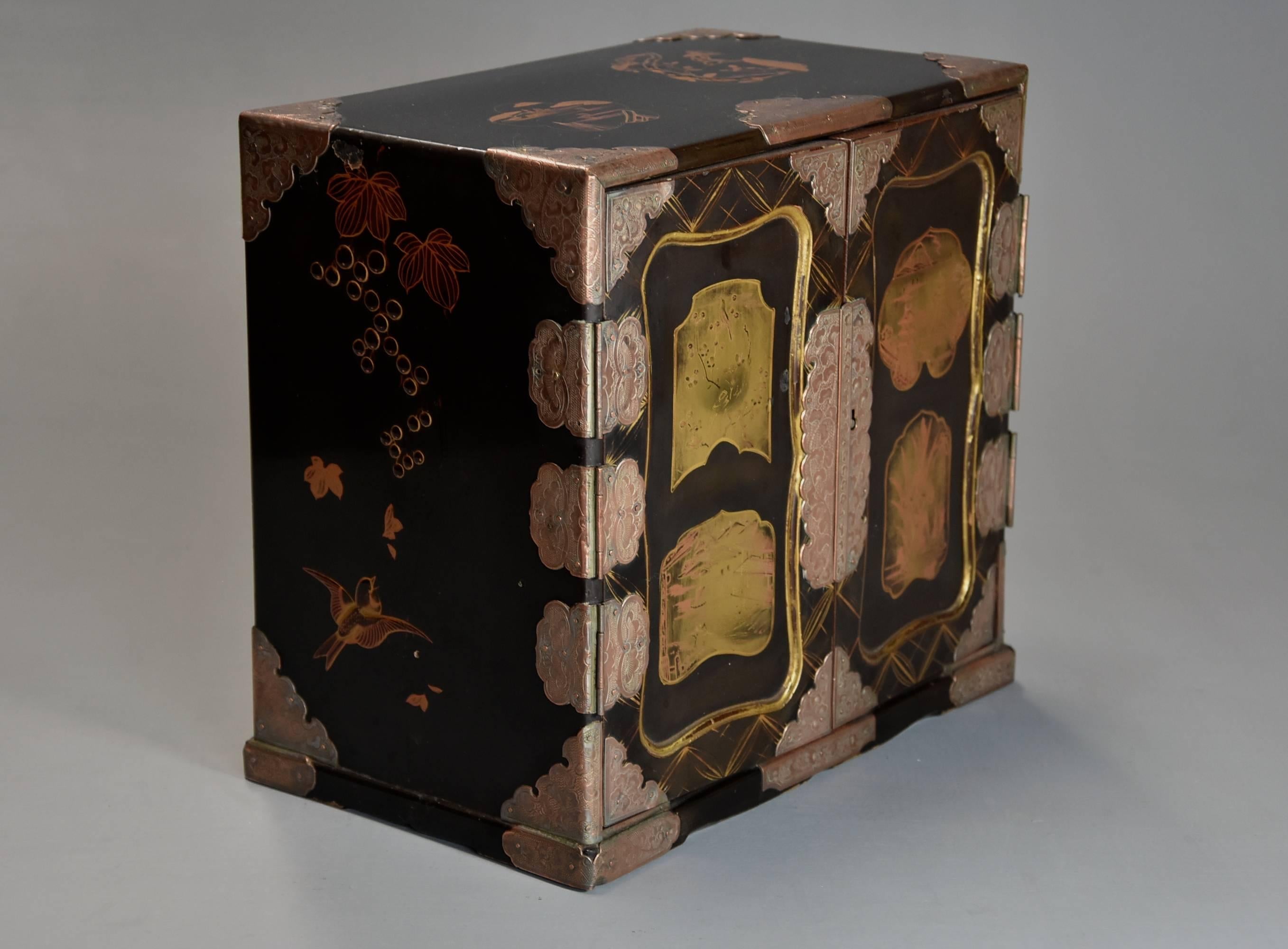 An early 20th century Japanese two-door lacquered table cabinet.

This table cabinet is lacquered with a black ground consisting of two doors to the front with elaborate metal mounts and escutcheon plates with shaped recessed panels with gilt