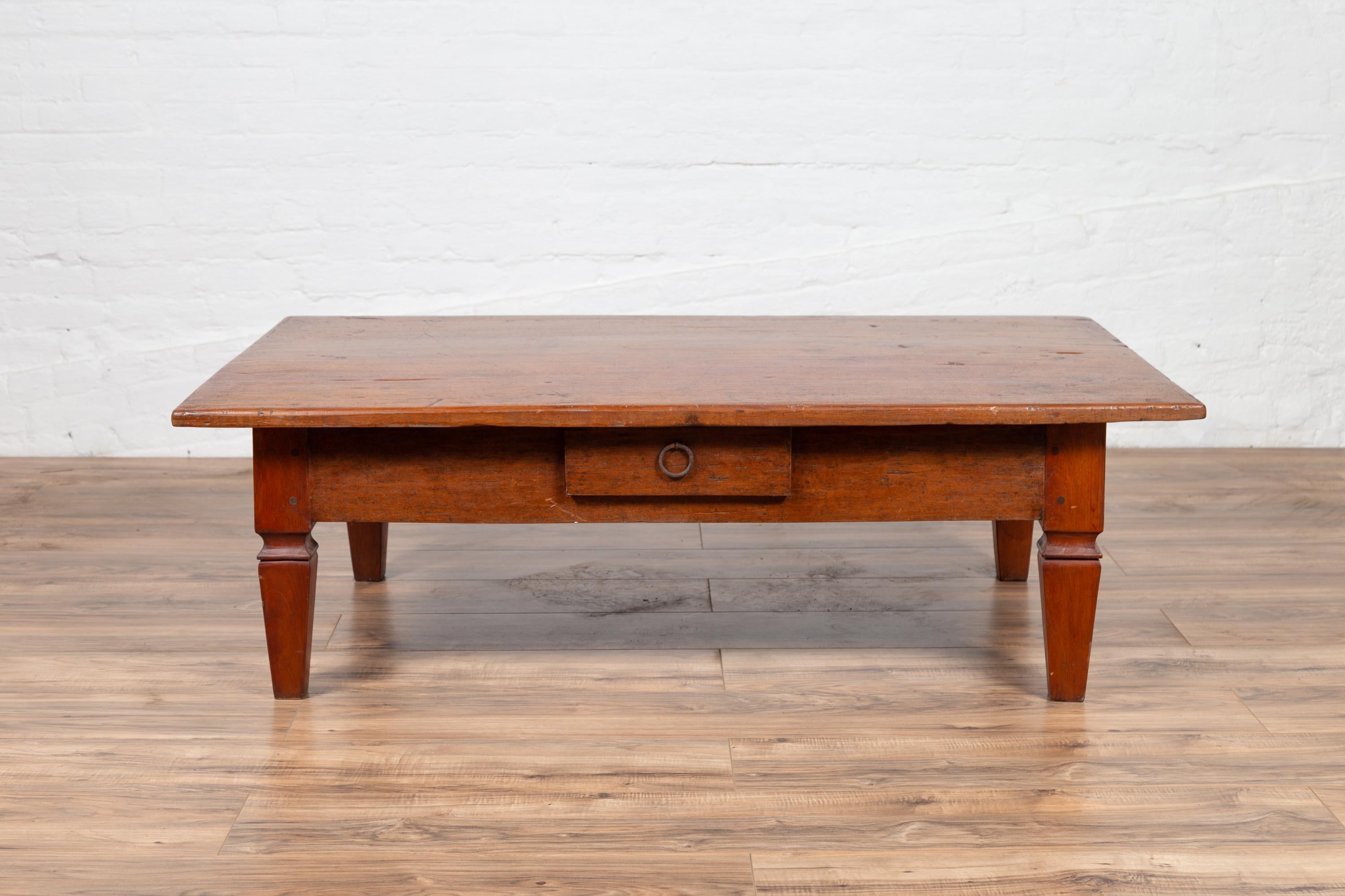 An antique Indonesian wooden coffee table from the early 20th century, with single drawer and tapered legs. Born on the island of Java during the early years of the 20th century, this charming coffee table features a rectangular single plank top,