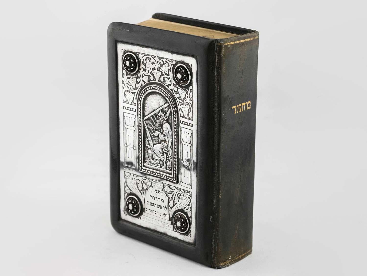 Machzor for Rosh Ha’Shana/Yom Kippur.
Leather binding with a silver on plaque cover by Bezalel Jerusalem. Depiction of King David with his Harp, set within frame of two ornamental arches with four applique bosses at corners. Additional grape design