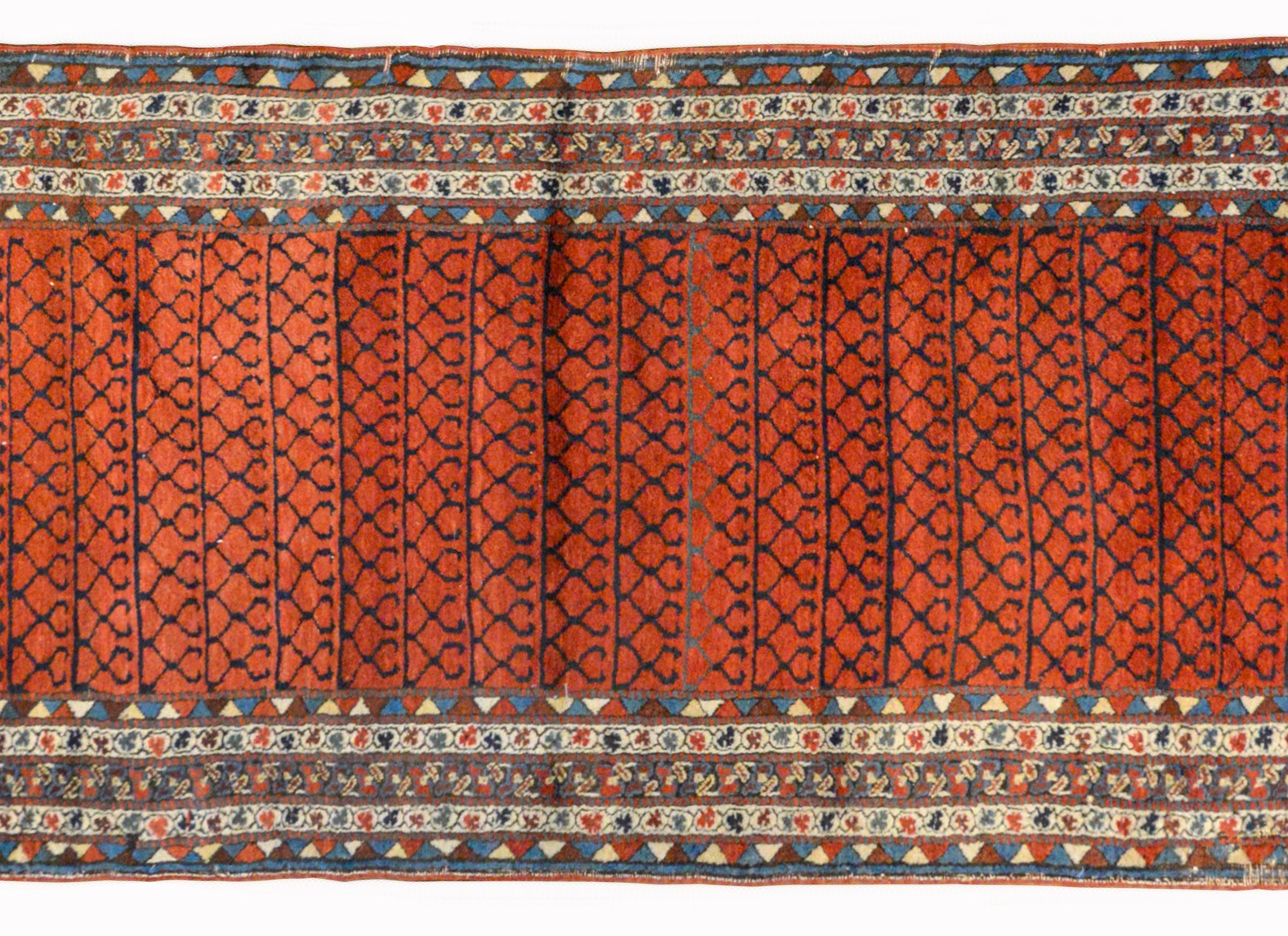 A gorgeous early 20th century Azerbaijani Karabak runner with a central field with a geometric trellis pattern woven in indigo against a rich crimson background. The border is extraordinary woven with multiple petite floral and striped patterned