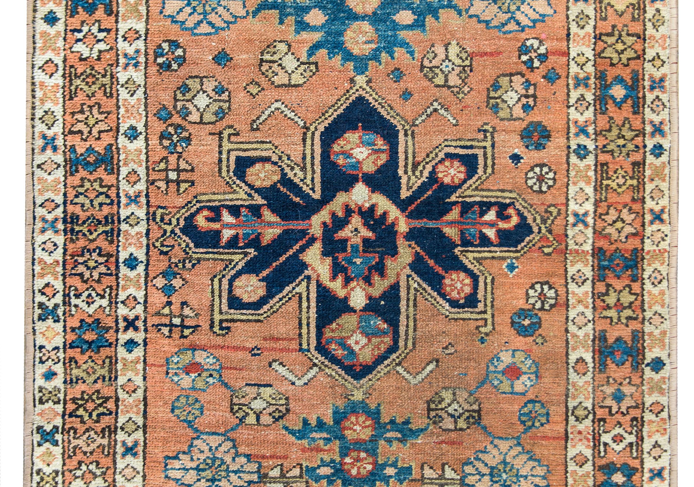 A beautiful early 20th century Persian Karadja rug with a stylized floral medallion living amidst a field of more stylized flowers and leaves, surrounded by a simple border of petite repeated stylized flowers, and all woven in indigo, gold, crimson,