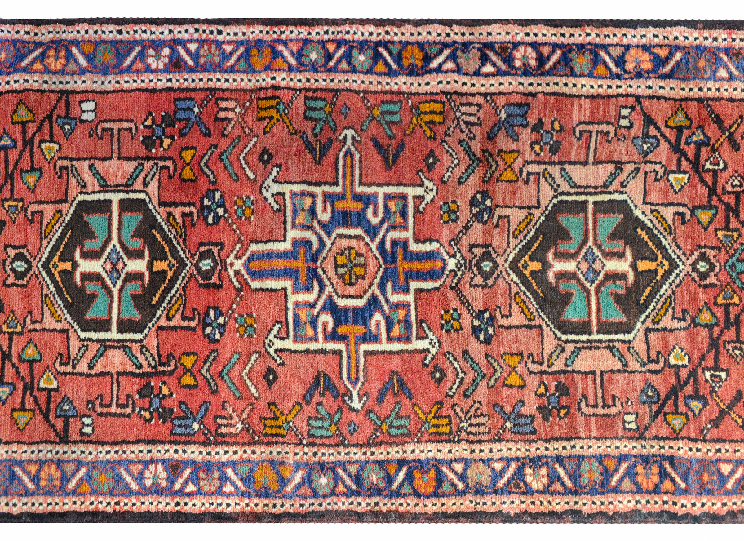 A wonderful early 20th century Persian Karadja runner with several stylized floral medallions woven in black, pink, light blue, gold, and green amidst a field of more stylized flowers against a coral red background. The border is wonderful composed