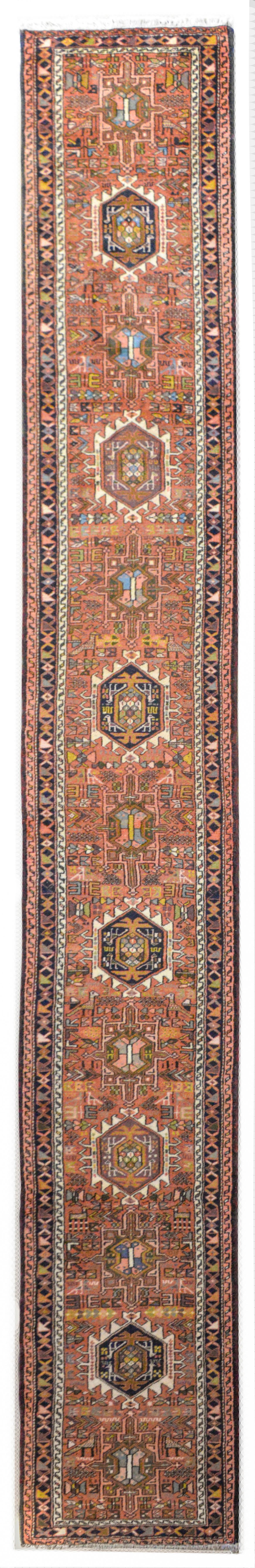 A wonderful early 20th century Persian Karadja runner with several stylized floral medallions woven in black, pink, light blue, gold, and green amidst a field of more stylized flowers against a coral red background. The border is wonderful composed