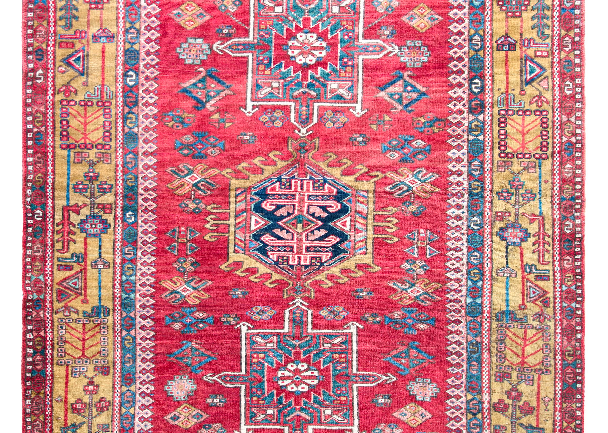 A striking early 20th century Persian Karaja rug with a tribal pattern containing three large central medallions heavily woven with stylized flowers, and living amidst a field of even more stylized flowers, surrounded by a wide border with a