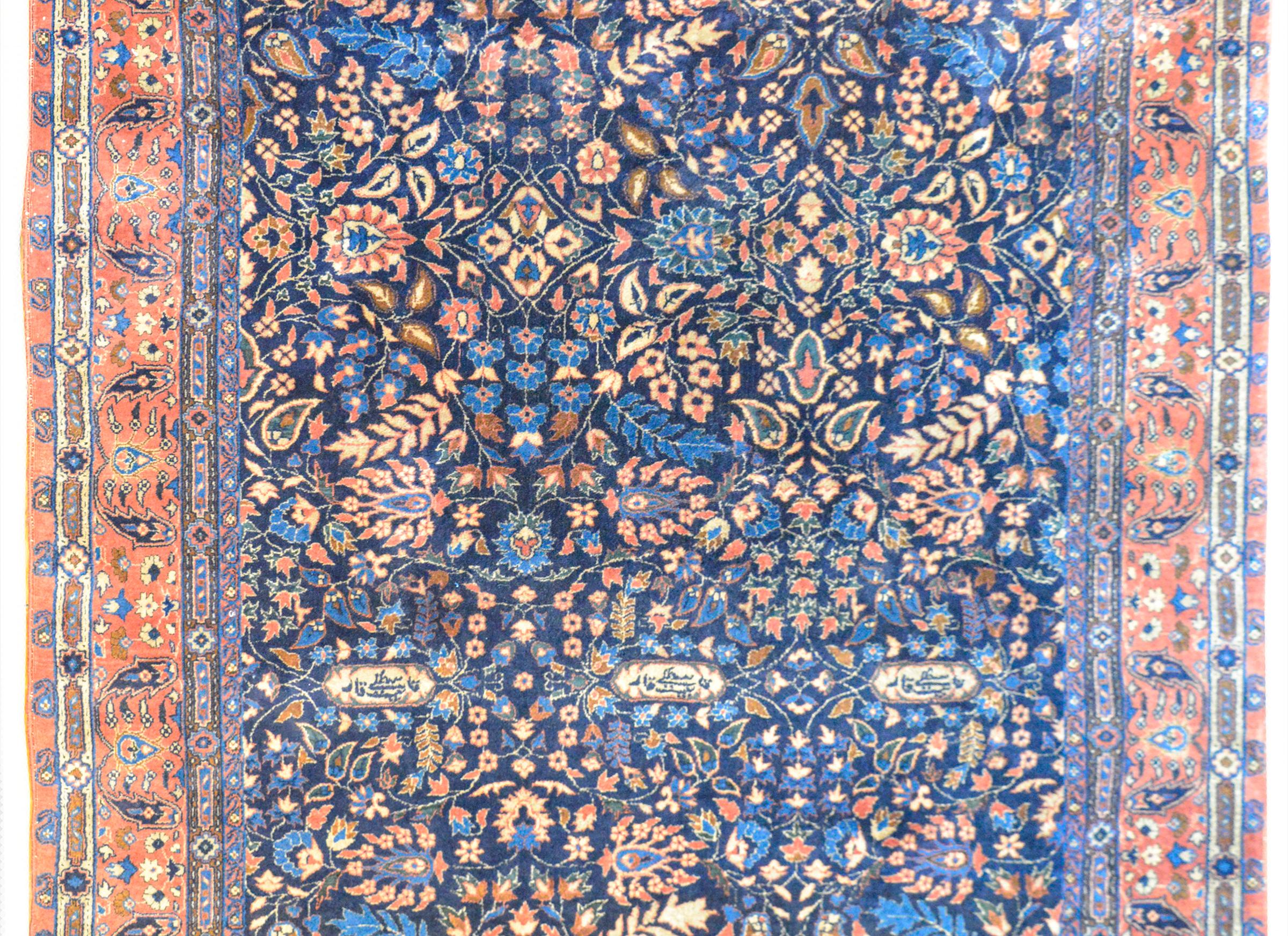 A wonderful early 20th century Indian Larastan rug with an all-over mirrored floral and scrolling vine pattern with myriad flowers and leaves woven in light and dark indigo, cream, brown, and coral against a dark indigo background. The border is