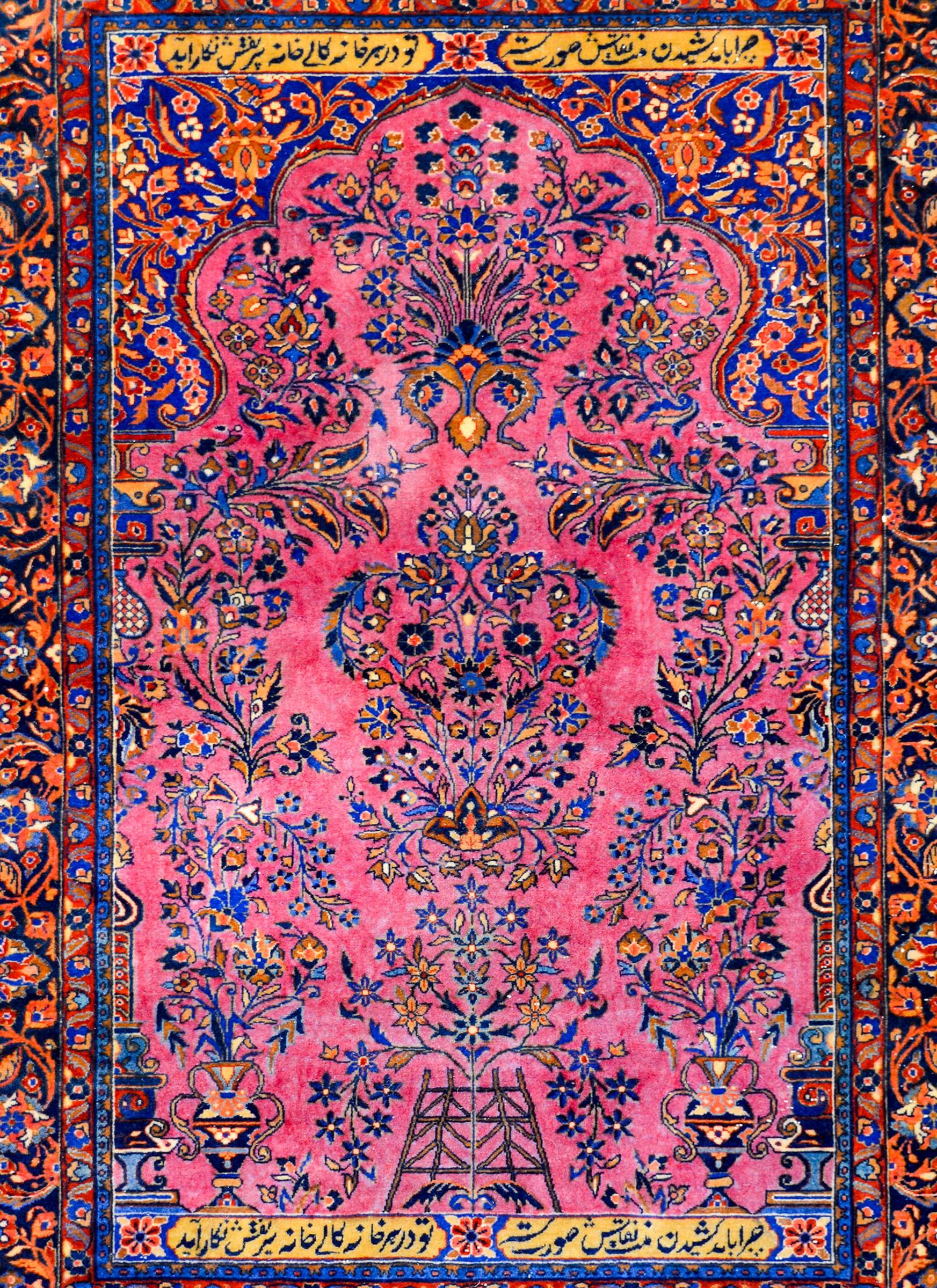 A wonderful early 20th century Persian Kashan prayer rug with a central tree-of-life pattern woven in light and dark indigo, orange, crimson, and gold vegetable dyed wool on a light cranberry colored field. The border is wide with a large-scale