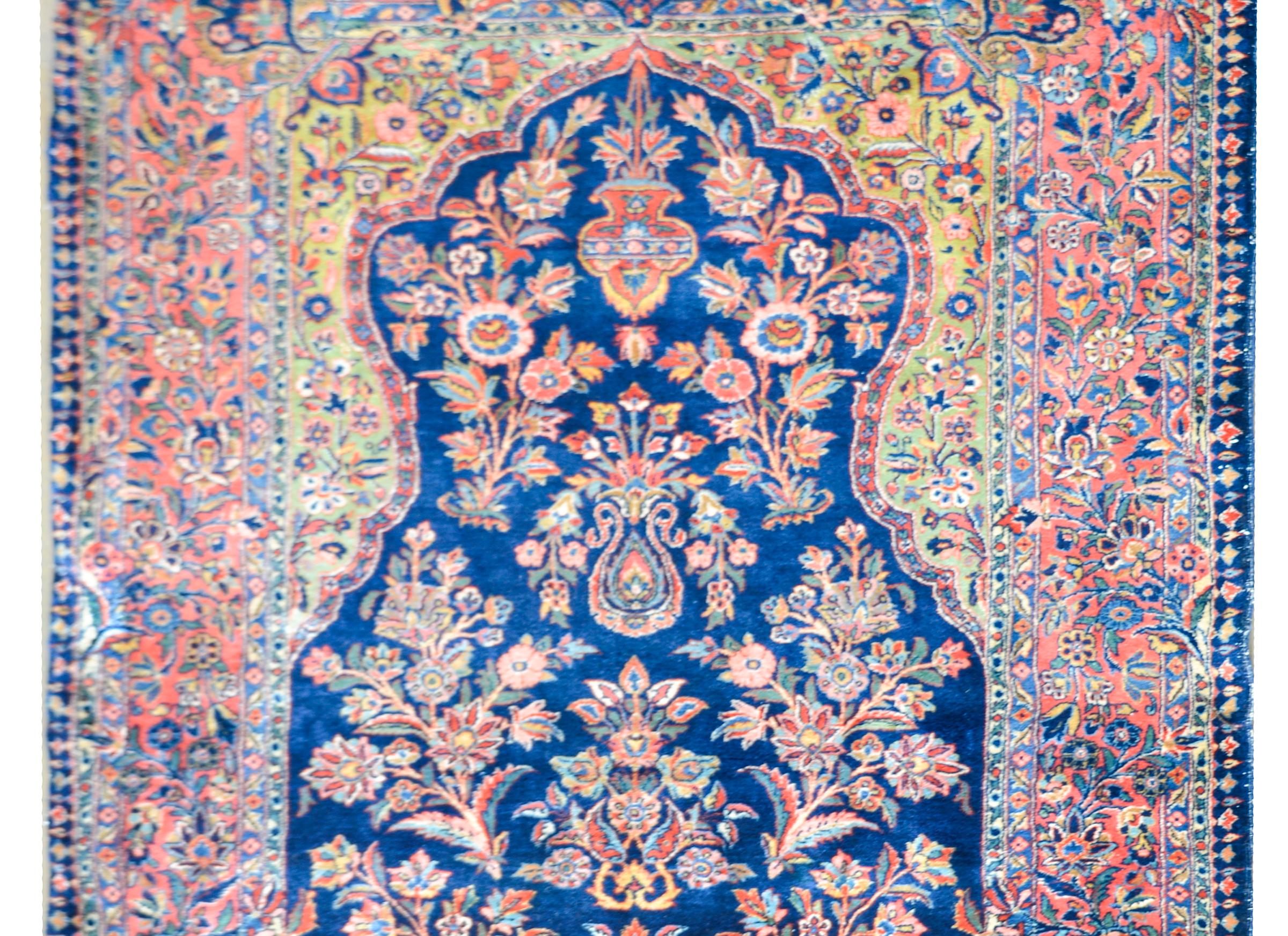 An early 20th century Persian Kashan prayer rug with a wonderful floral pattern woven in myriad colors including crimson, pink, gold and white, against a dark indigo background, and surrounded by an elaborately clustered floral patterned border