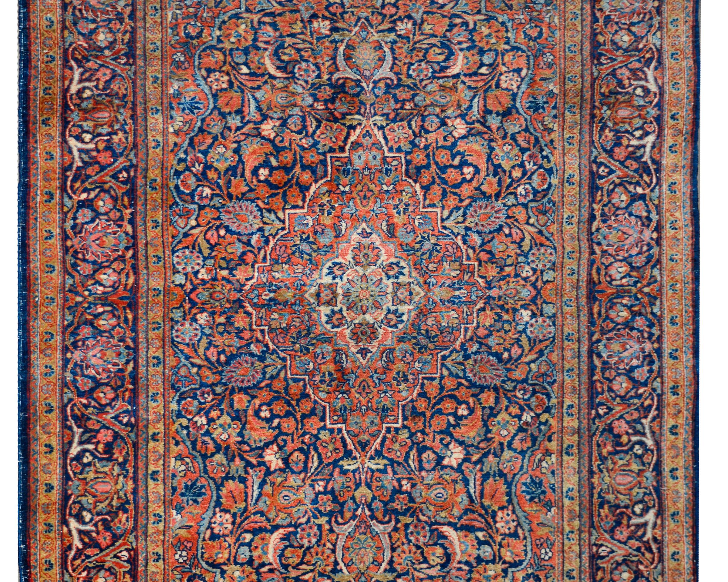 A stunning early 20th century Persian Kashan rug with a traditional central floral medallion living amidst a field of scrolling vines, leaves, and flowers, all woven in traditional Kashan colors of light and dark indigo, crimson, gold, and cream,