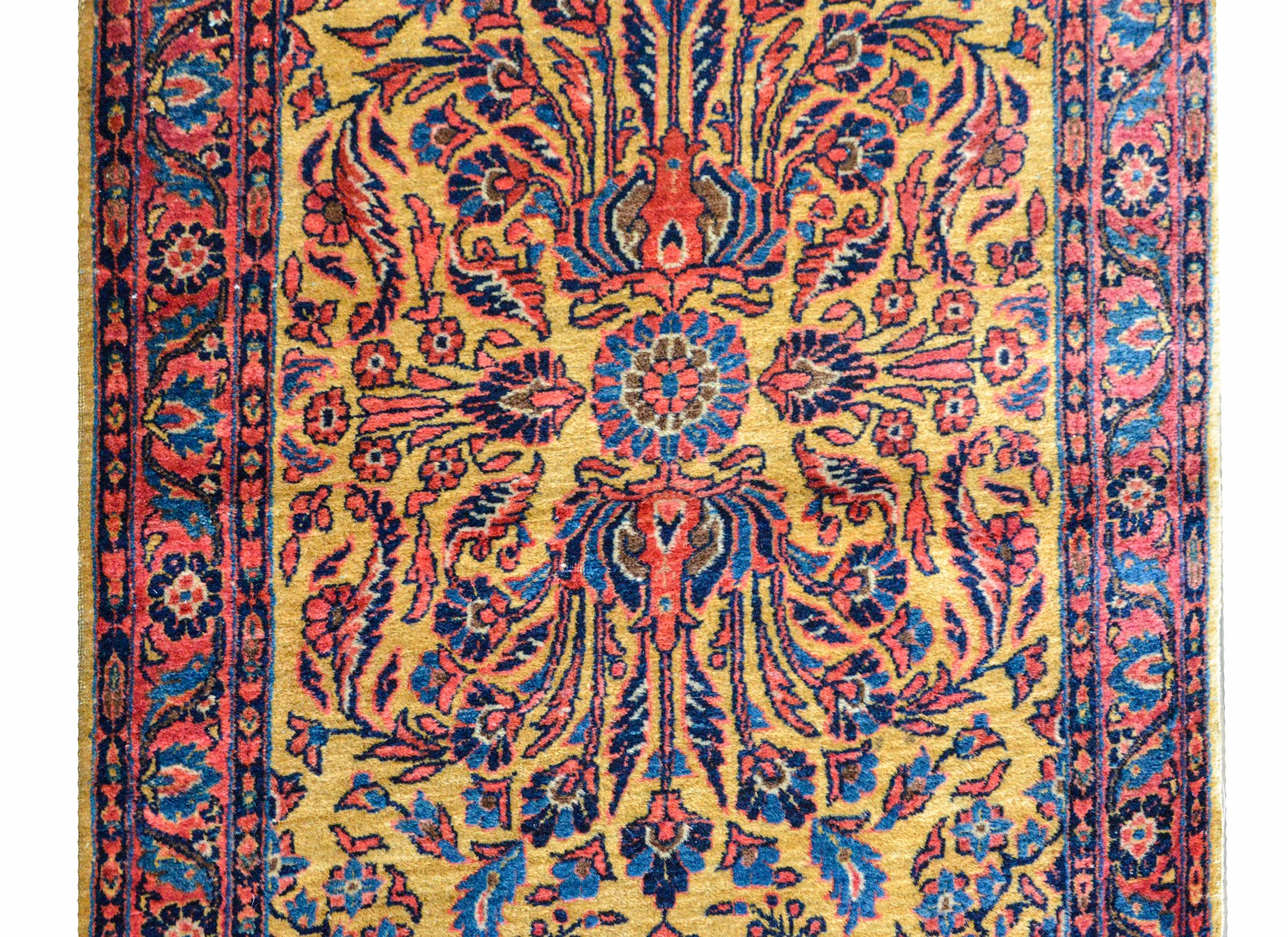 A beautiful early 20th century Persian Kashan runner with a fantastic large-scale floral pattern with scrolling leaves, flowers, and vines, all woven in light and dark indigo and pink against a rich gold background, and surrounded by a wide floral