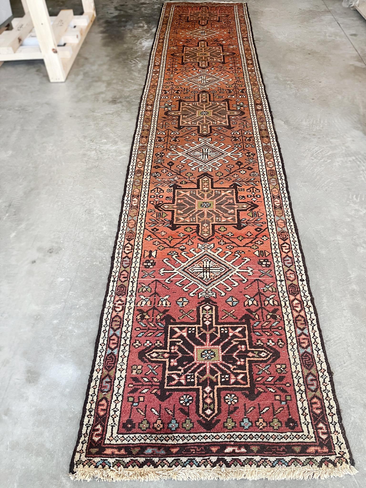 Esta alfombra larga kazaka se tejió a principios del siglo XX. Tiene una paleta terrosa de marrón rojizo, marfil, negro, verde y rosa. El diseño presenta un campo rojo central con una columna de medallones en medio de un intrincado grupo de motivos