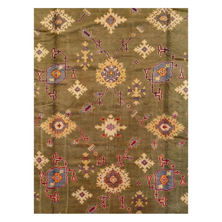 An antique Turkish Oushak large oversized carpet handmade during the early 20th century with a dominating khaki green field. An all-over pattern of various half-rosettes and 'guls' (flowers) fill the, otherwise, open field very much in the style of
