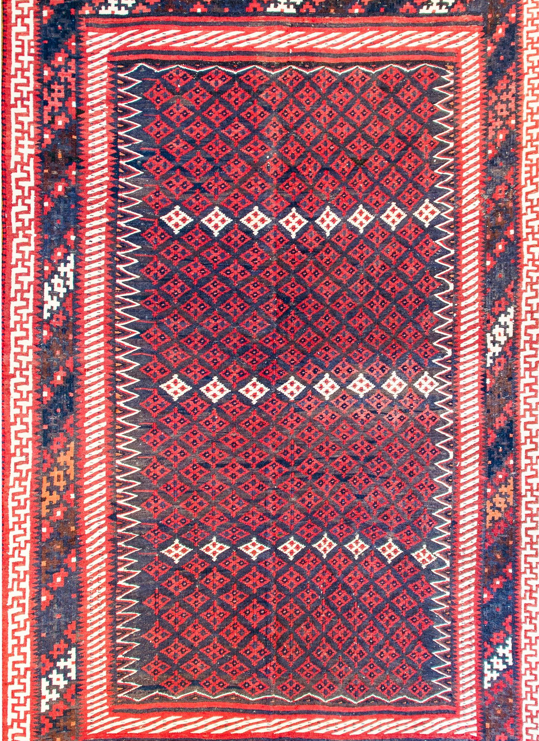An early 20th century Persian Khorasan Sumak rug with an all-over crimson diamond pattern with three rows of white diamonds, on an indigo background. The border is complex with four distinct geometric patterns woven in crimson, indigo, white, and