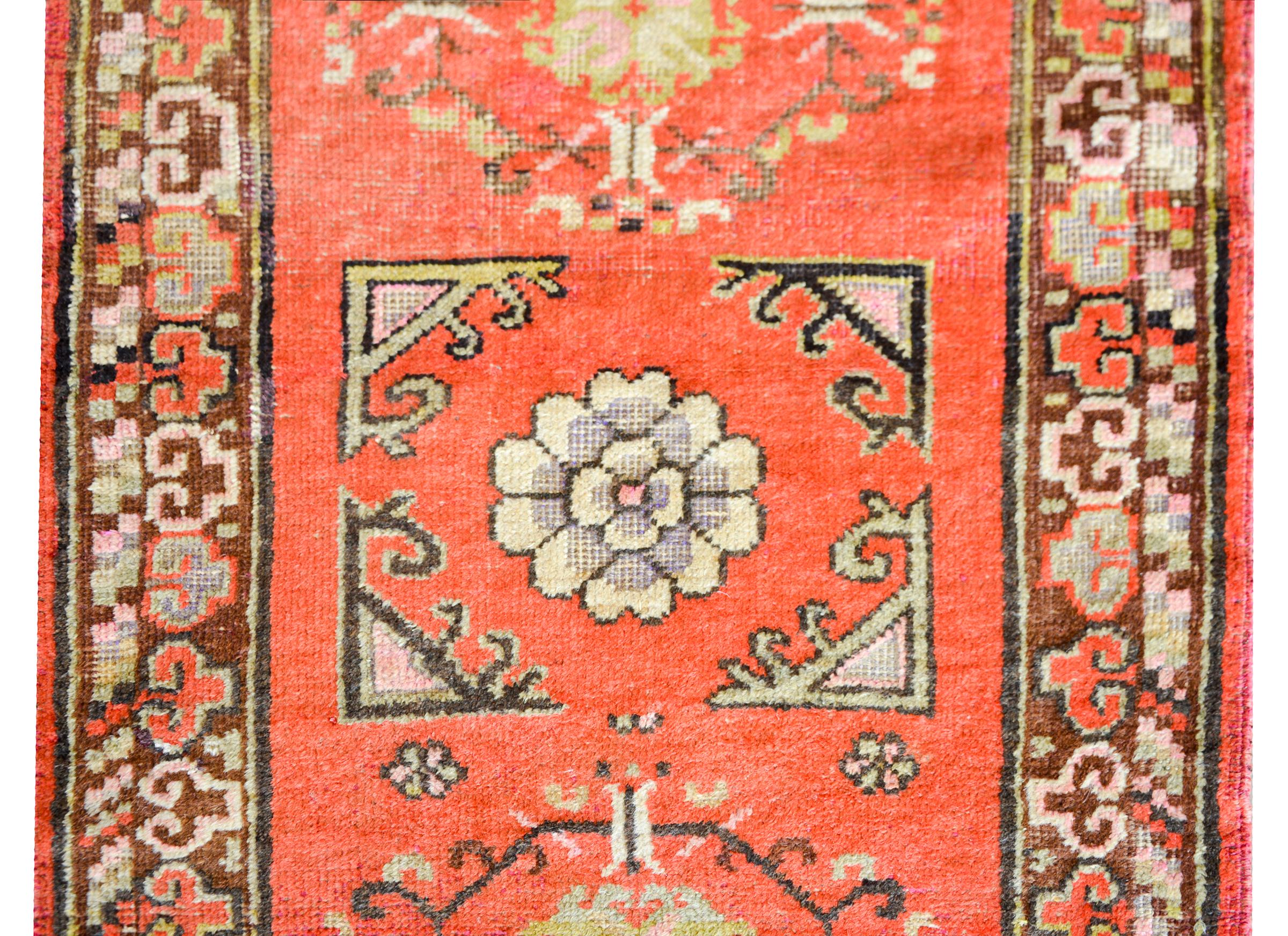 A beautiful early 20th century East Turkestan Khotan rug with several medallions with stylized flowers woven in muted colors inducing gold, crimson, pink, and brown against a coral colored background, and surrounded by a border with a stylized