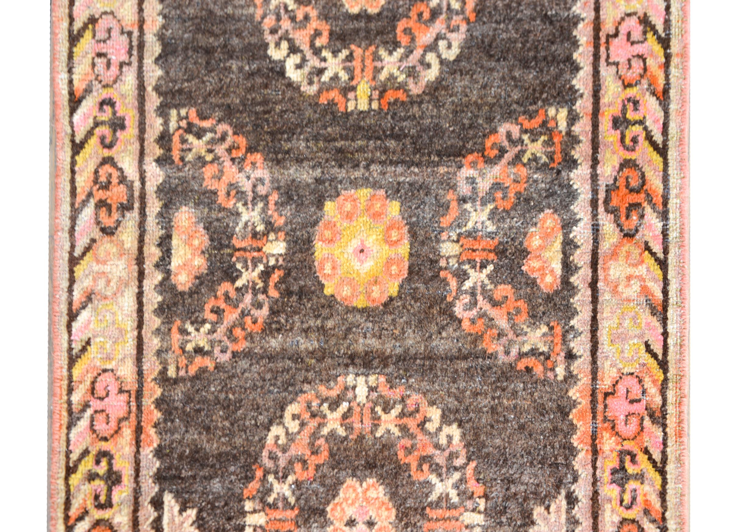 A petite and sweet early 20th century Central Asian Khotan rug with two floral medallions woven in coral, white, gold, and gray wool against a black background and surrounded by a border woven with a turbulent cloud patterned border woven in similar