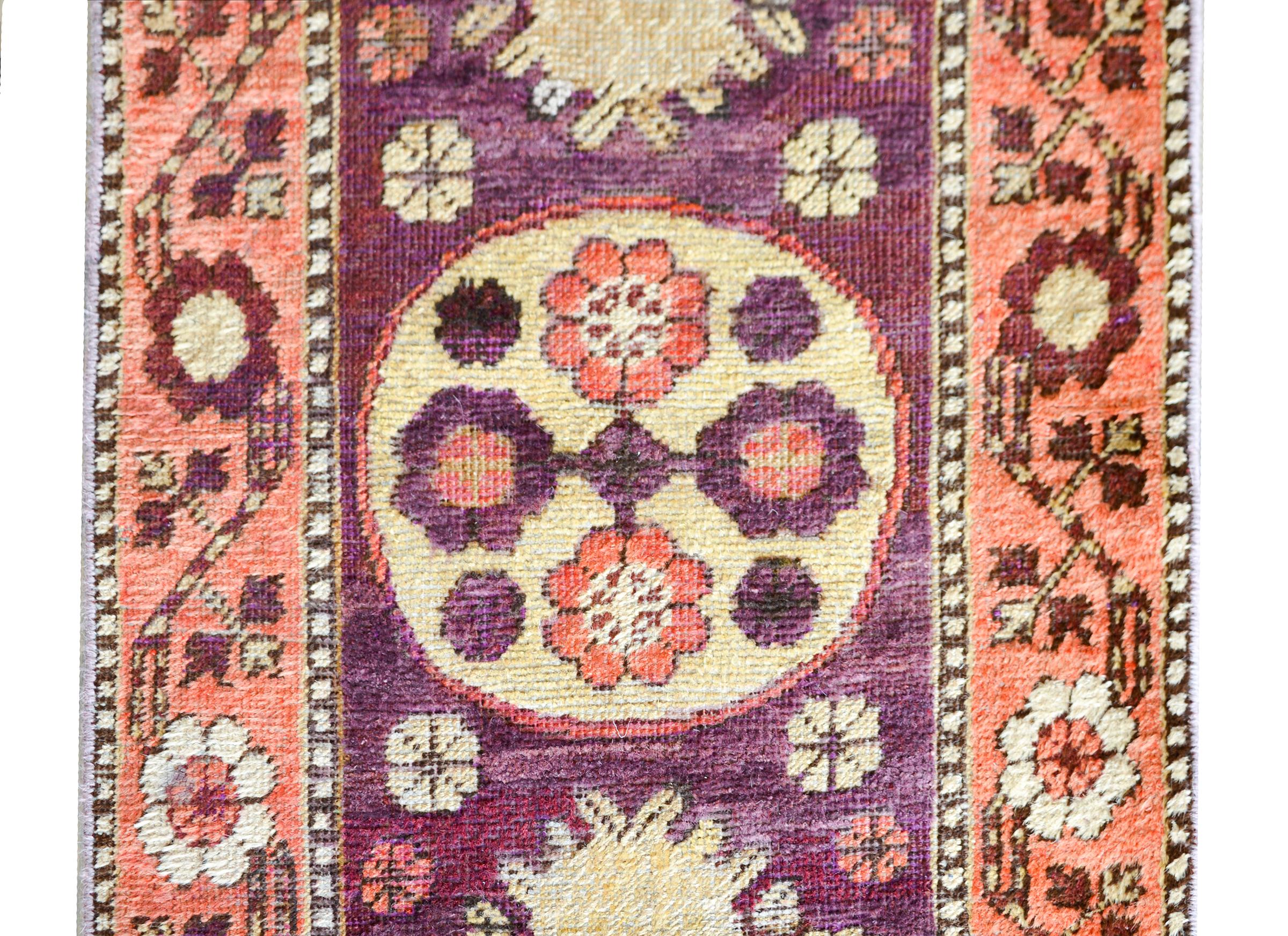 An early 20th century Central Asian Khotan runner with three wonderful large medallions with stylized floral clusters amidst a field of more stylized flowers against a dark violet background and surrounded by a border containing more flowers and