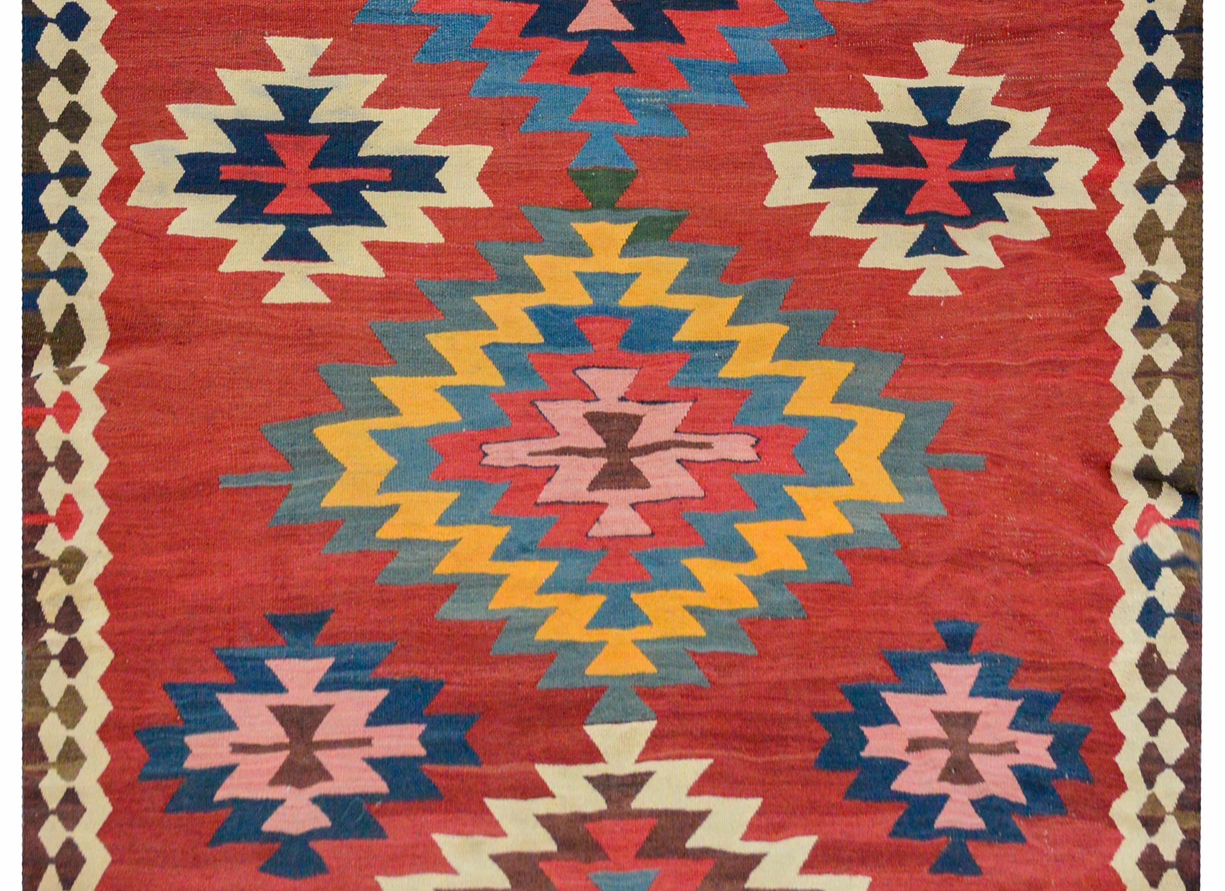A wonderful early 20th century Persian Kilim runner with a bold pattern containing eight large stylized floral medallions amidst a field of smaller stylized flowers all on an abrash crimson background. The border is simple with a brown and white
