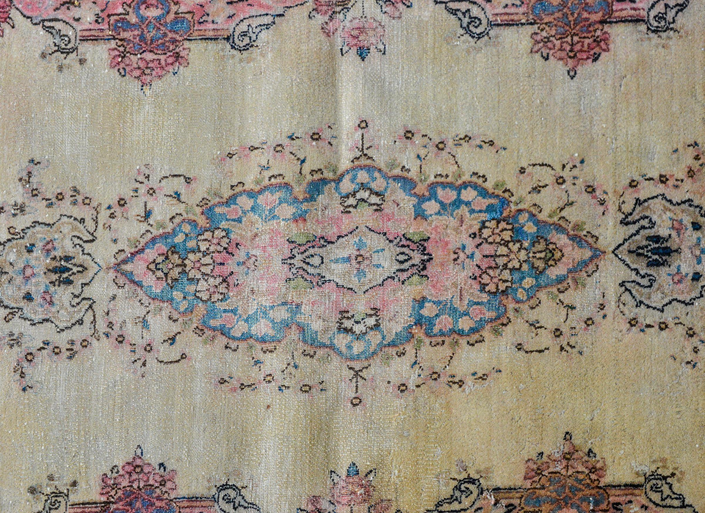 An unusual early 20th century Persian Kirman rug with a long ovoid central floral medallion woven in light indigo plink and cream, against a solid champagne, and surrounded by a wide floral patterned border.