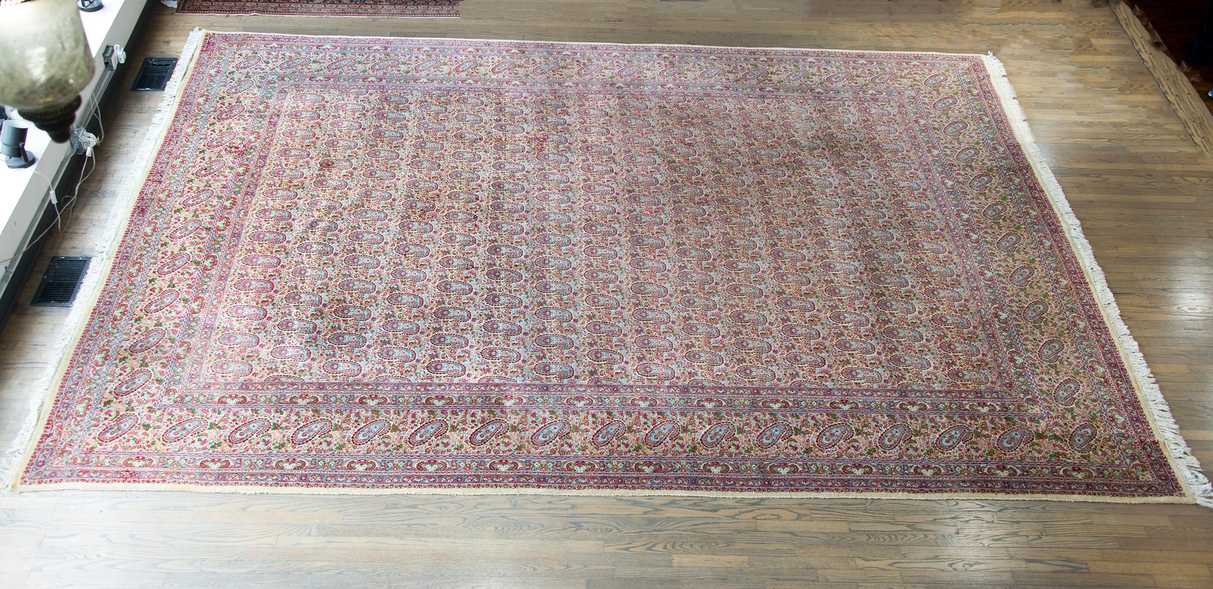 A gorgeous early 20th century Persian Kirman rug with an all-over paisley and petite floral pattern woven in traditional Kirman colors including pinks, cranberries, light and dark indigo, and golds, and all framed by a matching large paisley pattern.