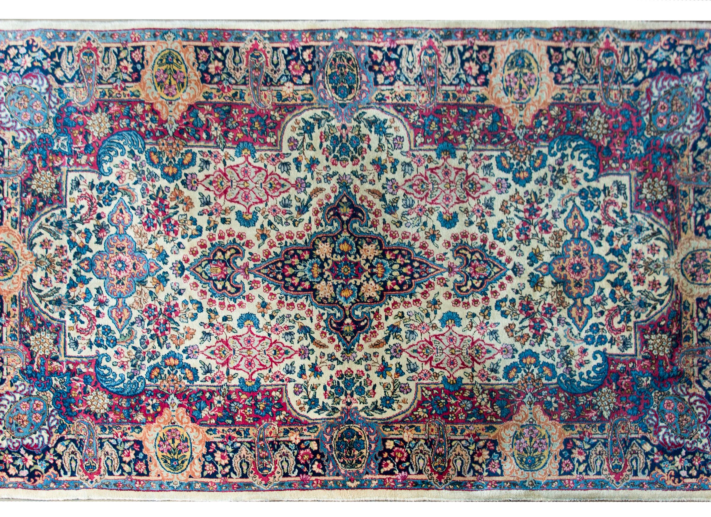 Ein schöner persischer Kirman-Teppich aus dem frühen 20. Jahrhundert mit einem traditionellen, spiegelnden Blumenmuster in leuchtenden Rosa-, Indigo-, Gold-, Grün- und Cremetönen, umgeben von einer breiten Bordüre mit weiteren Blumenmustern.
