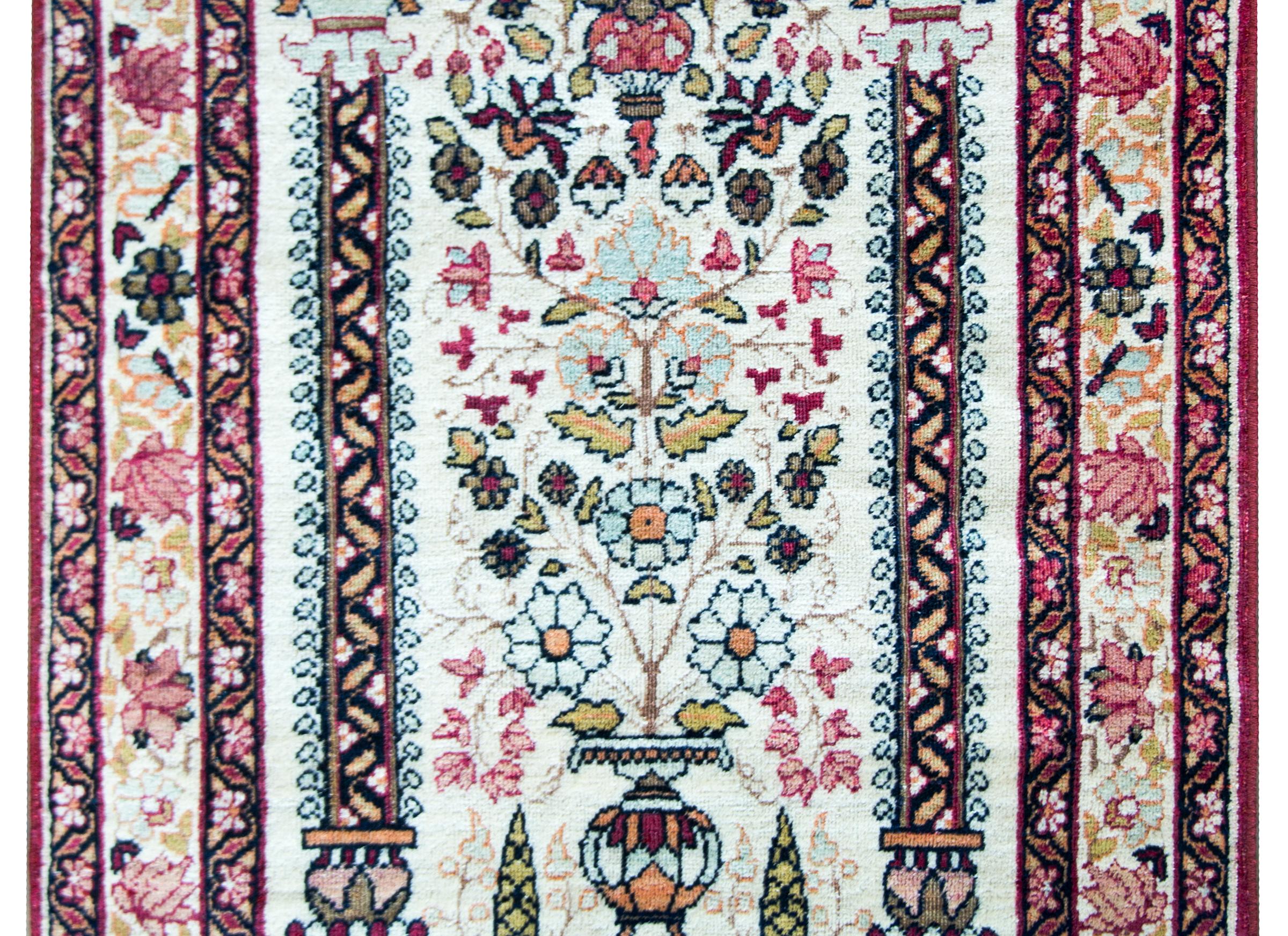 A wonderful early 20th century Persian Kirman rug with a vibrant central tree-of-life motif with several varieties of flowers potted in a vase and flanked by a pair of architectural columns, and all completely surrounded by a wonderful border