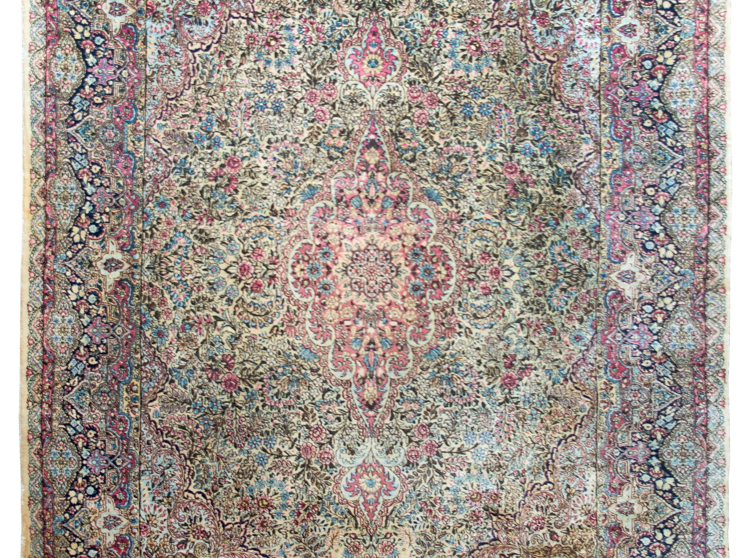 Una fascinante alfombra persa Kirman de principios del siglo XX, con un elaboradísimo diseño de innumerables flores y enredaderas, todo ello tejido en los colores tradicionales de Kirman: crema, distintos tonos de añil, rosa, arándano, dorado y