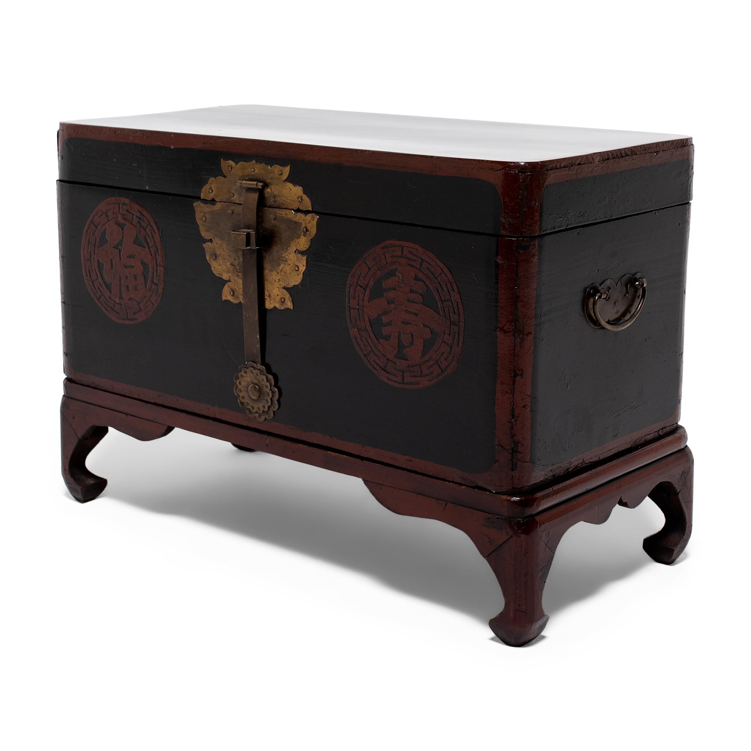 This lacquered wedding chest dates to the early 20th century and was likely originally used as a bridewealth chest during a traditional Korean wedding ceremony. The exterior is finished with red and black lacquer and decorated with two round
