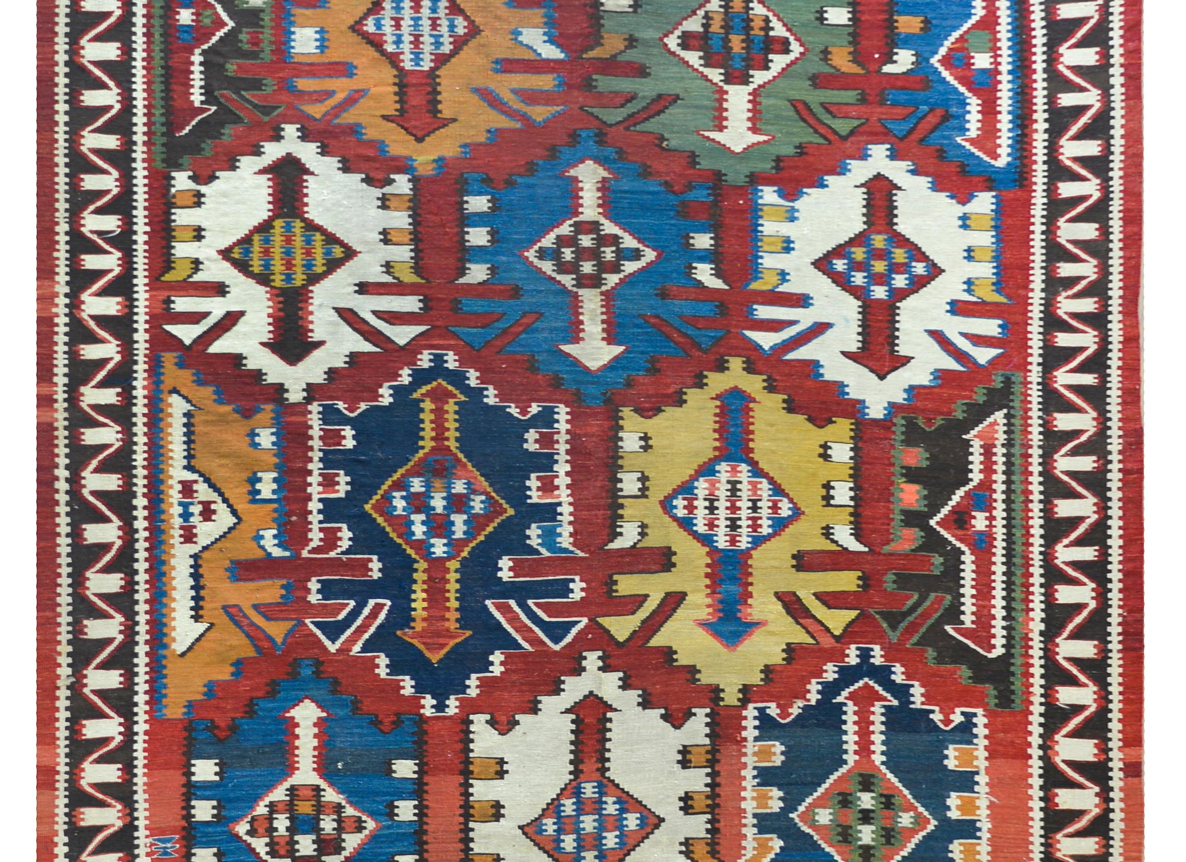 A rare and stunning early 20th century Persian Kuba kilim rug with a striking large-scale muli-colored stylized floral pattern against a crimson background, and surrounded by a striped border.