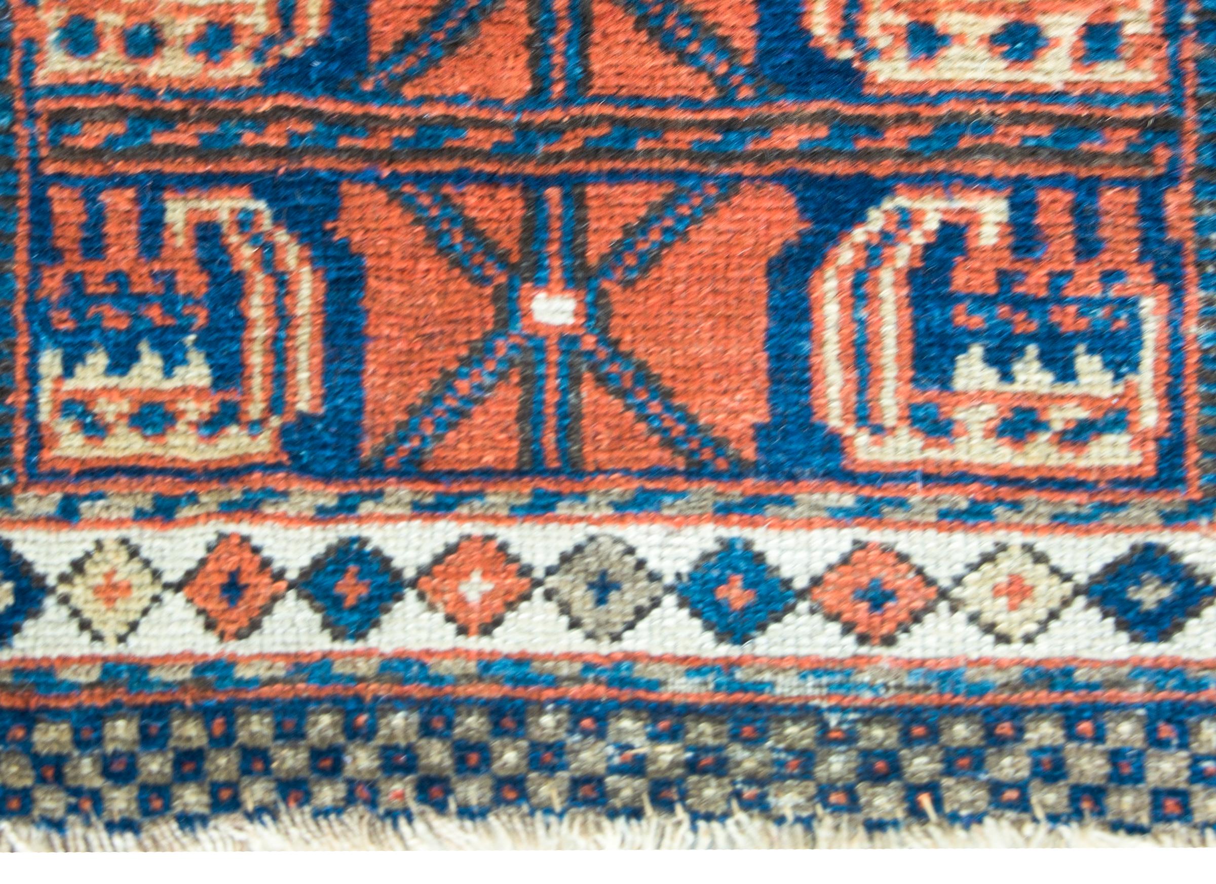 A beautiful early 20th century Kurdish bag face rug with a simple but modern pattern containing two large crimson stylized flowers and leaves set against an indigo background.  The border is simple with a petite diamond pattern.