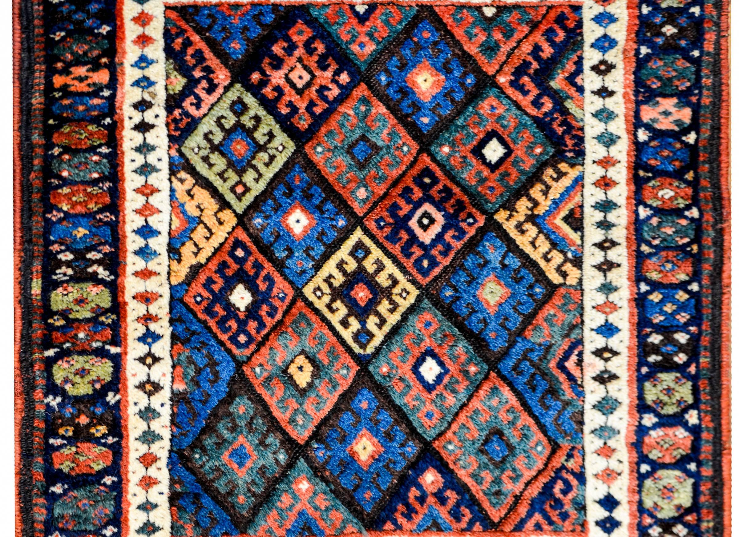 A wonderful early 20th century Kurdish Jaff rug with a complex pattern containing multiple diamonds with stylized flowers woven in crimson, indigo, green, black, and yellow colored wool. The border is complex, with two wide stripes, one with a