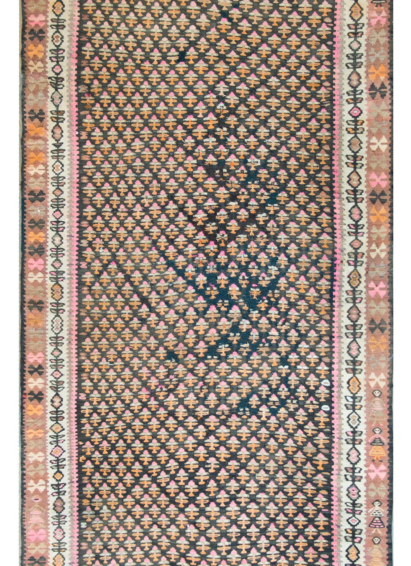 An incredible early 20th century Kurdish Kilim rug with an all-over stylized tree-of-life pattern woven in pink, orange, and cream colors wool, set against a black ground, and framed by a complex border containing several geometric patterned borders.