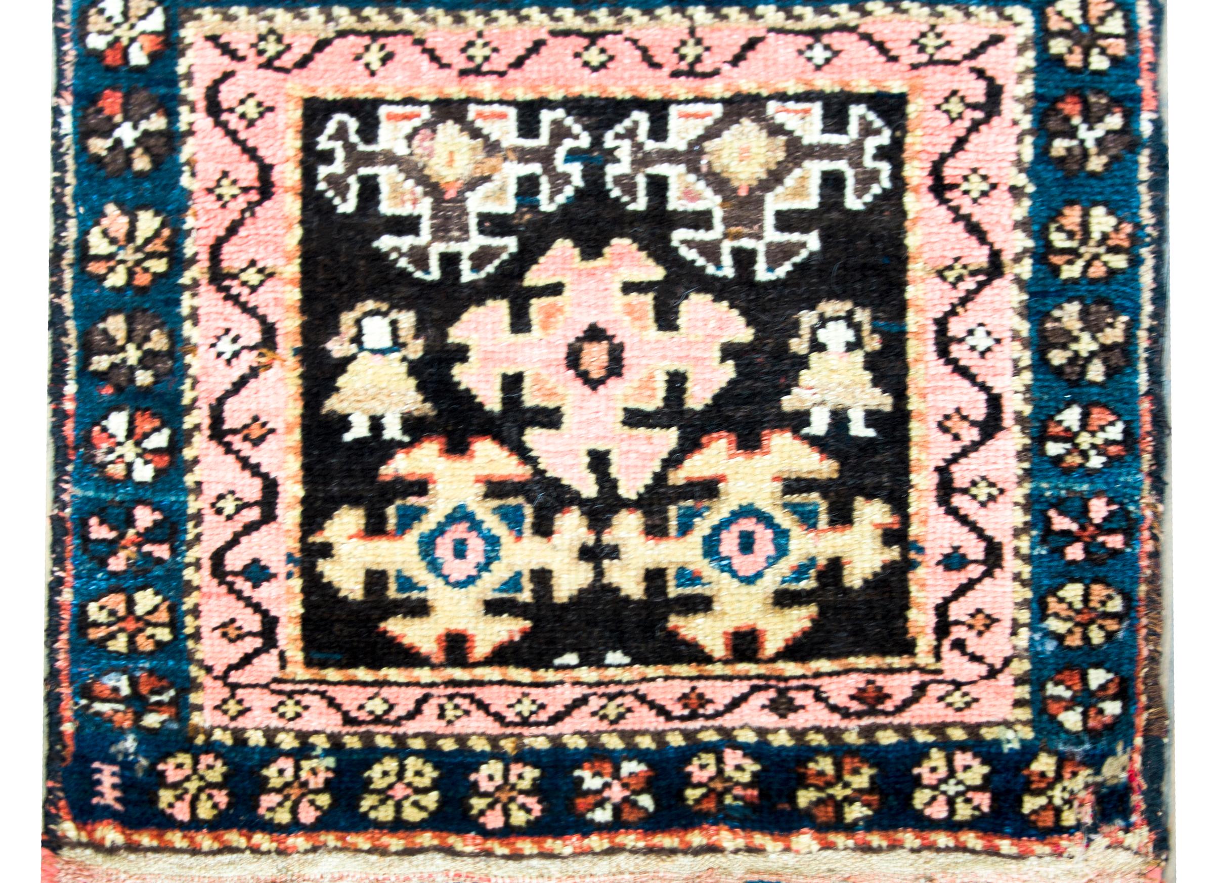 A striking early 20th century Kurdish rug with several stylized flowers woven in pink, yellow, and indigo, set against a black background, and surrounded by a border containing two stylized flor patterned stripes woven in similar colors as the field.