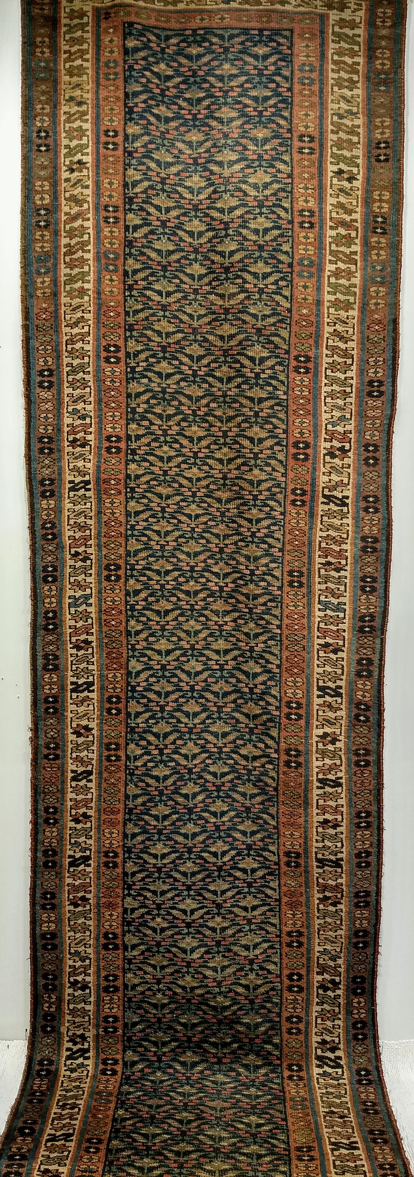 Corredor kurdo persa de principios del siglo XX, con un estampado de cachemira sobre fondo azul.  El motivo del campo es una variación de la forma paisley en colores marrón, rojo y verde enmarcada por tres bordes con diseños geométricos en colores