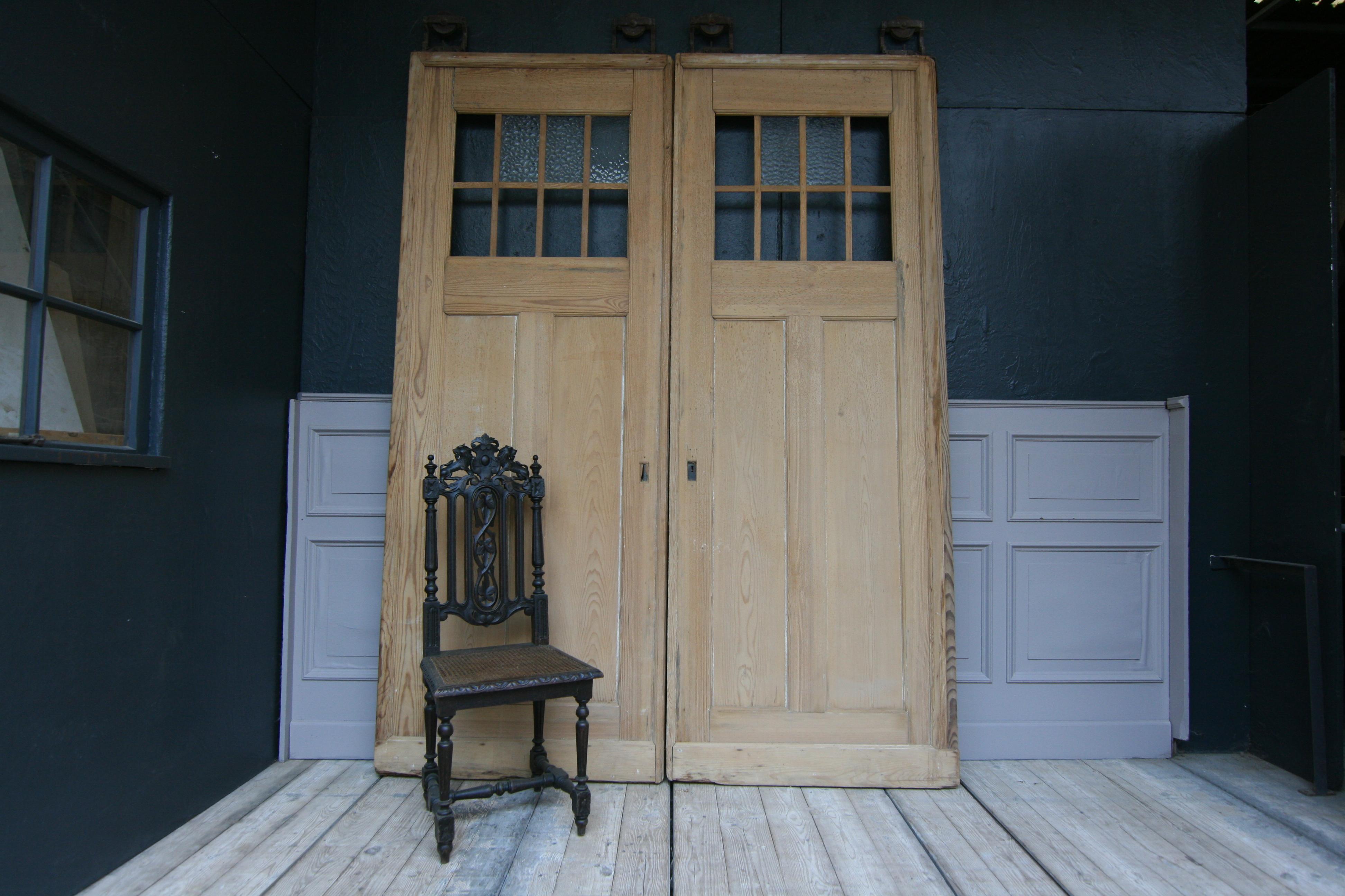 A pair of large early 20th century German doors made of pine.
Each door has the original bracket or rollers mounted on top with which they could originally be used as sliding doors.
The pine wood is leached, so the doors can now be refurbished as