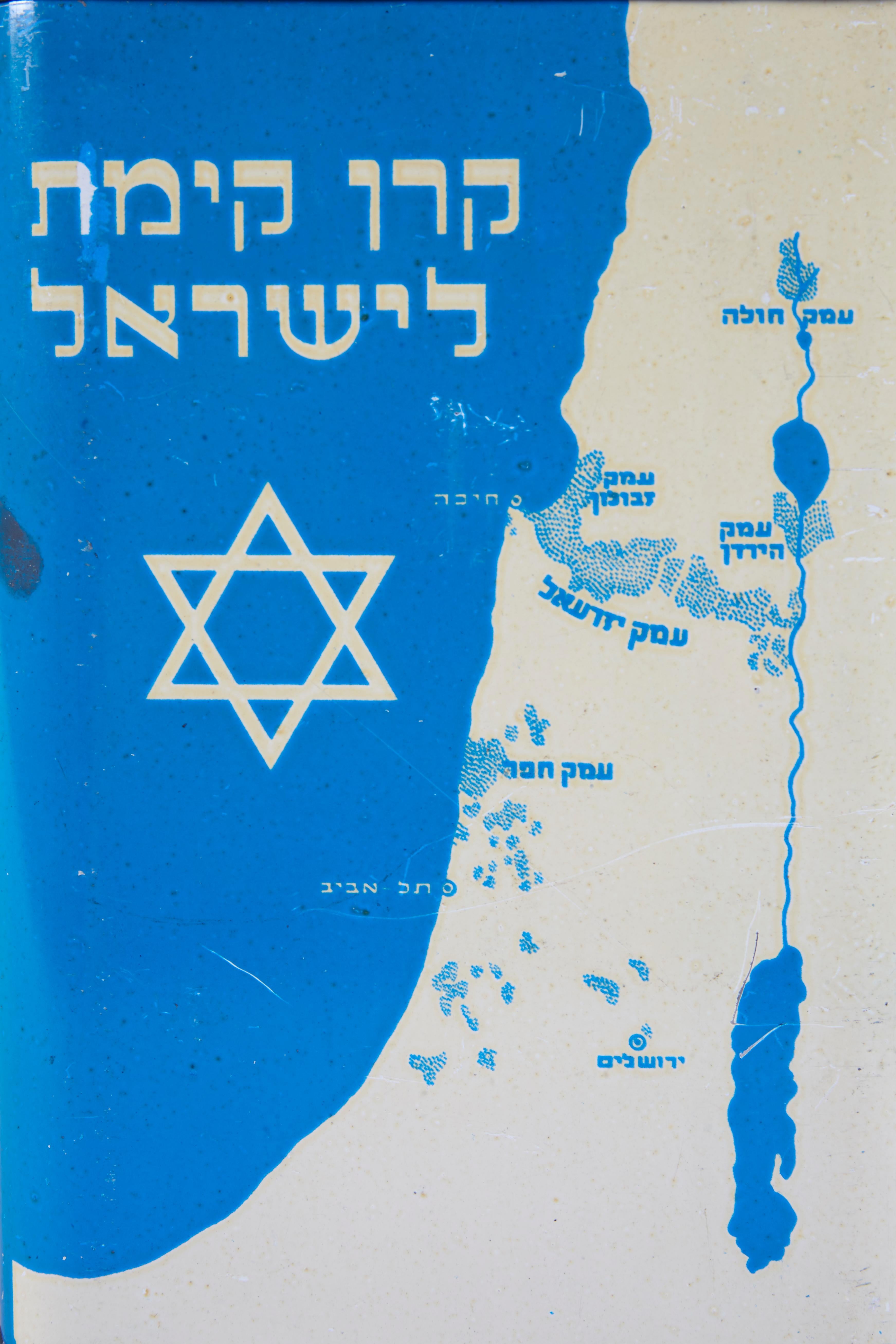Painted blue and white tin charity box, circa 1925. 
Decorated with a Star of David and the map of Israel in Hebrew on one side, and KKL for Keren Kayemet Yisrael, spelled out in Hebrew, on the other side with a handle for collecting.
Marked on the
