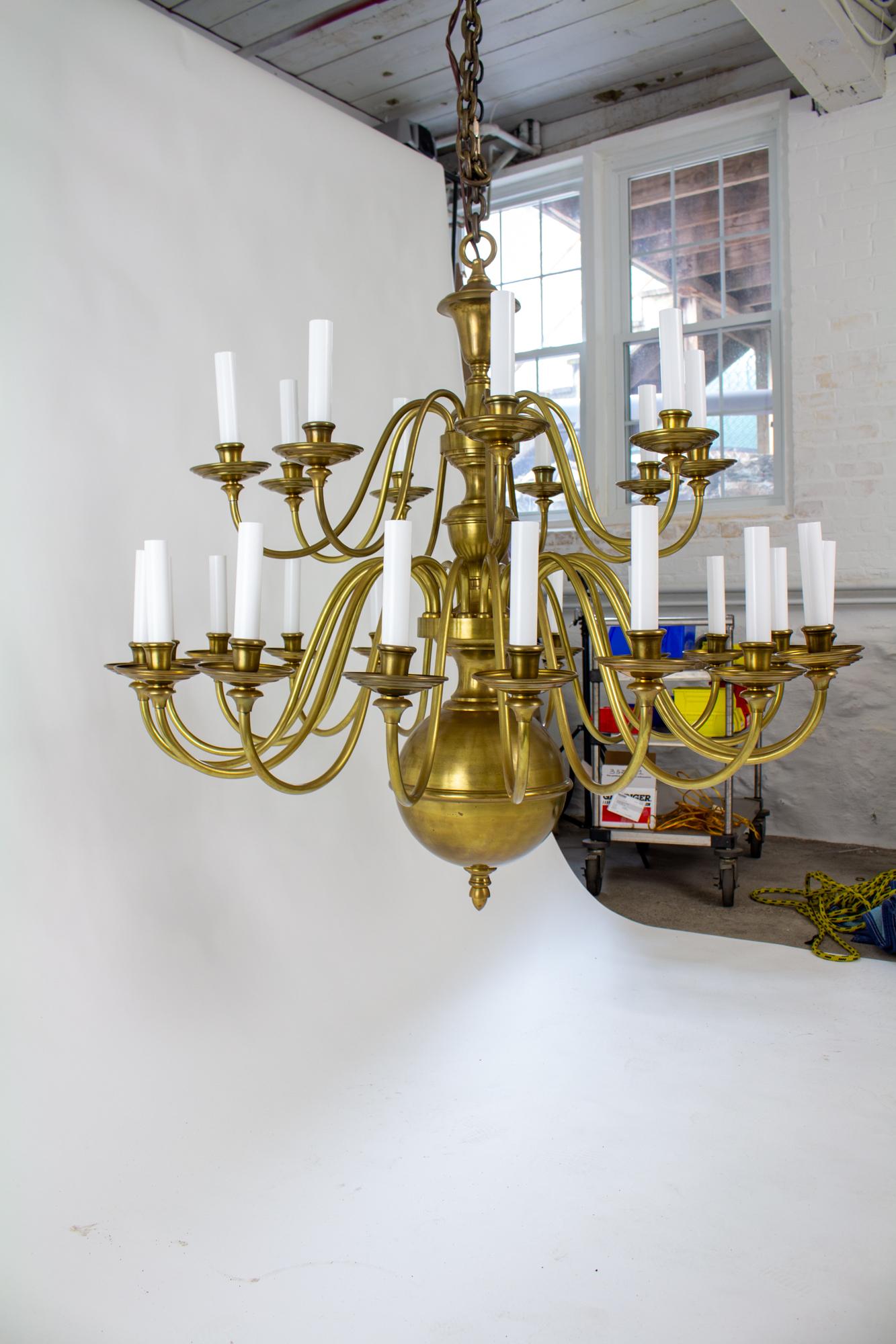 Early 20th Century large two tier colonial style brass chandelier. The scale of this chandelier is appropriate for a great room, barn, or other large space. The top tier has nine arms and the bottom tier has 18 arms. The central stem is made of