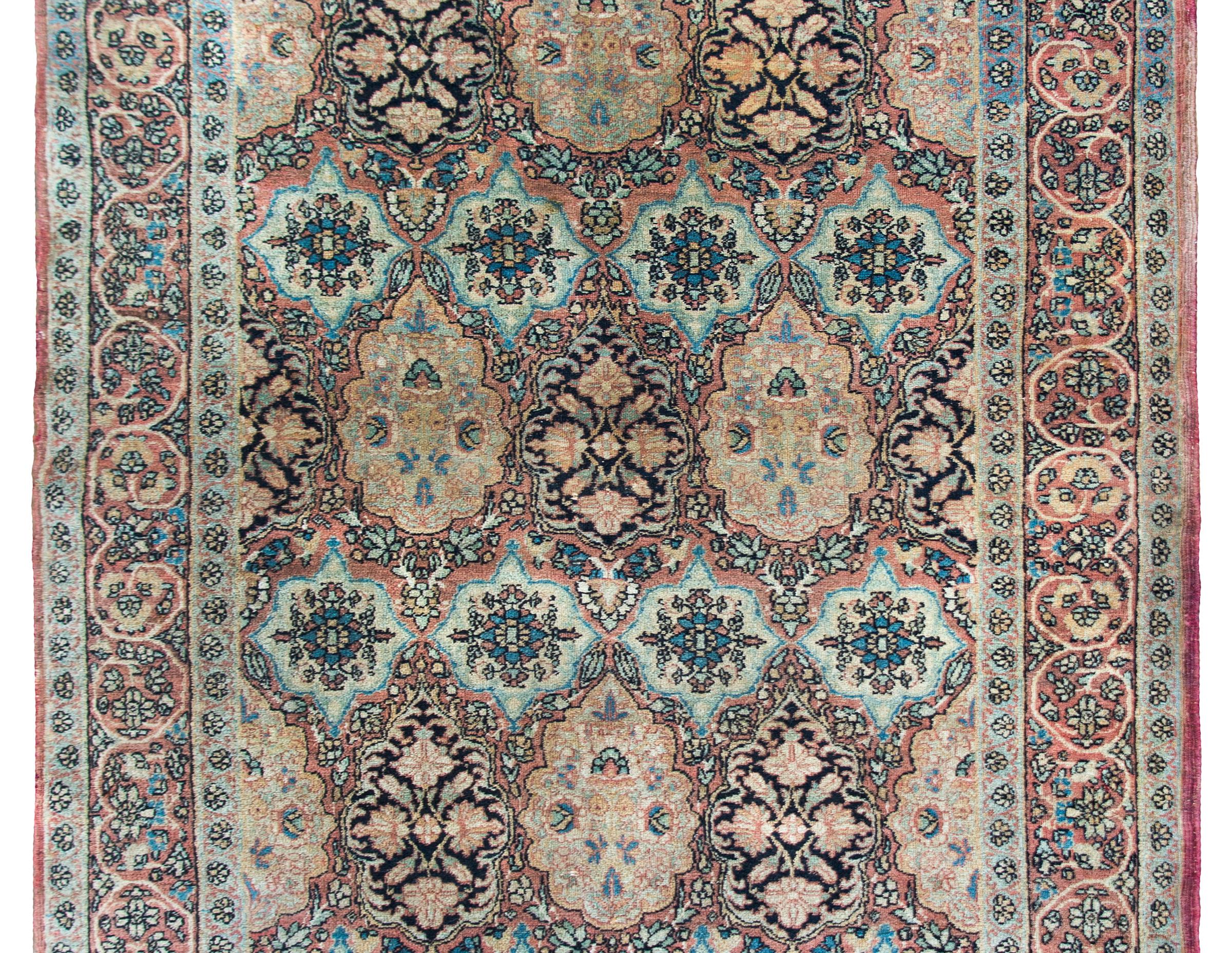 A wonderful early 20th century Persian Lavar Kirman rug with several floral medallions covering the field, surrounded by a wide border with more flowers and scrolling vines, and all woven in muted indigos, reds, oranges, yellows, and creams.