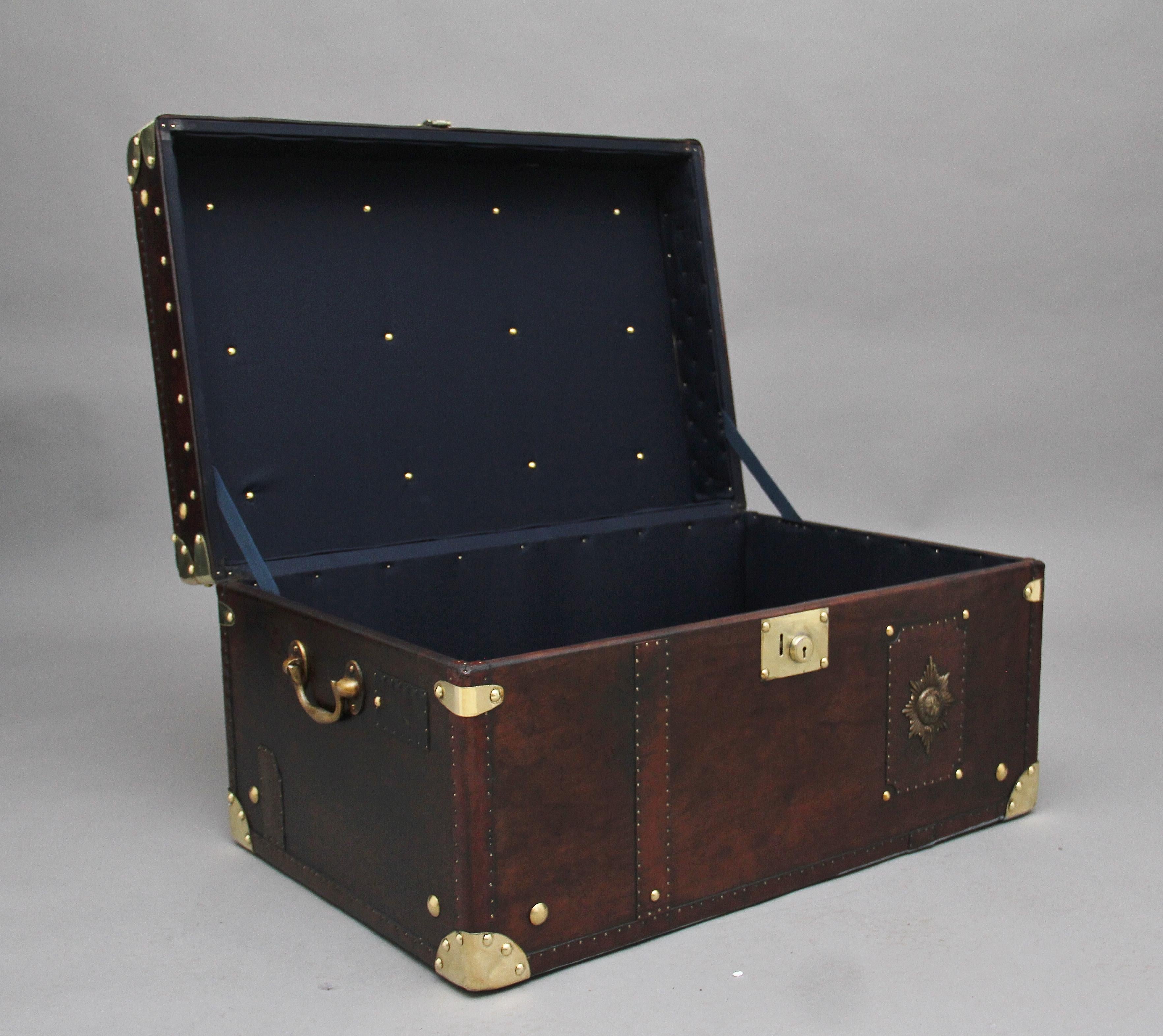 A fabulous early 20th century leather bound ex army trunk with brass straps and corners, copper studs and brass carrying handles on the sides, the trunk opens to reveal a nice dark blue lined interior, on the front of the trunk there is the