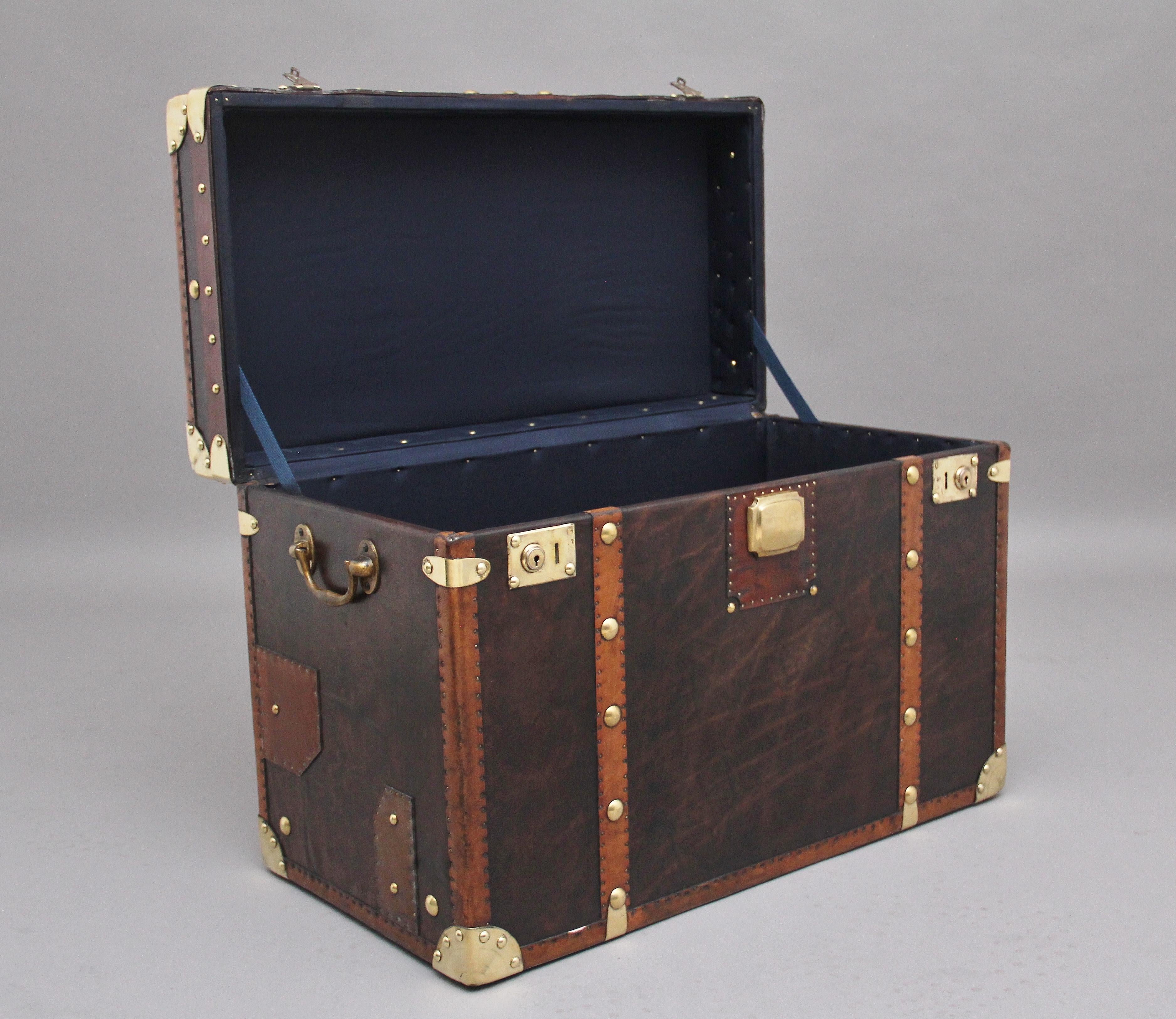 Early 20th century leather bound ex army trunk with brass straps and corners, copper studs and brass carrying handles on the sides, the trunk opens to reveal a nice dark blue lined interior, on the top of the trunk there is the regimental badge
