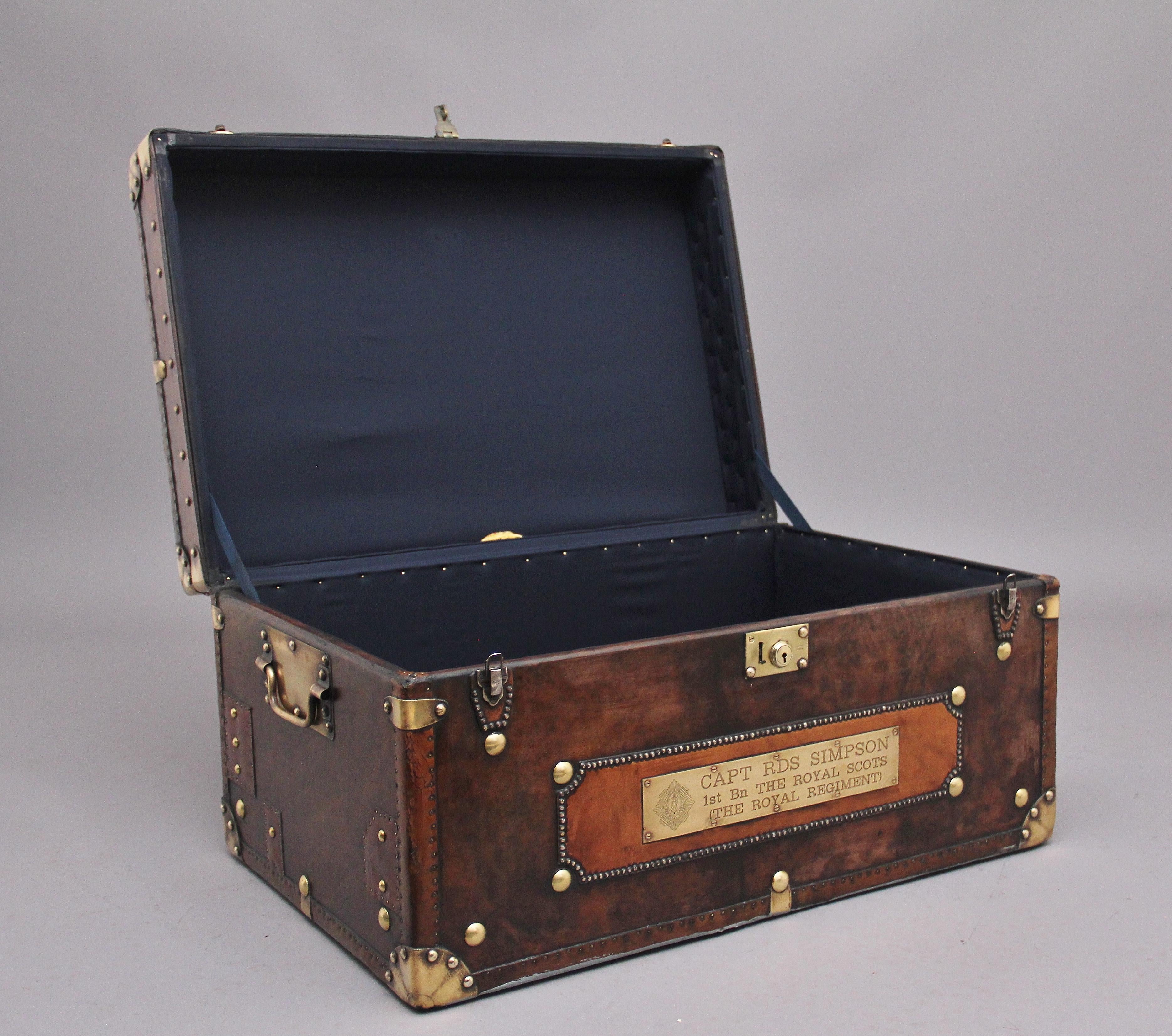 An early 20th century leather bound ex army trunk with brass straps and corners, copper studs and brass carrying handles on the sides, the trunk opens to reveal a nice dark blue lined interior, on the front of the trunk there is a brass plaque which
